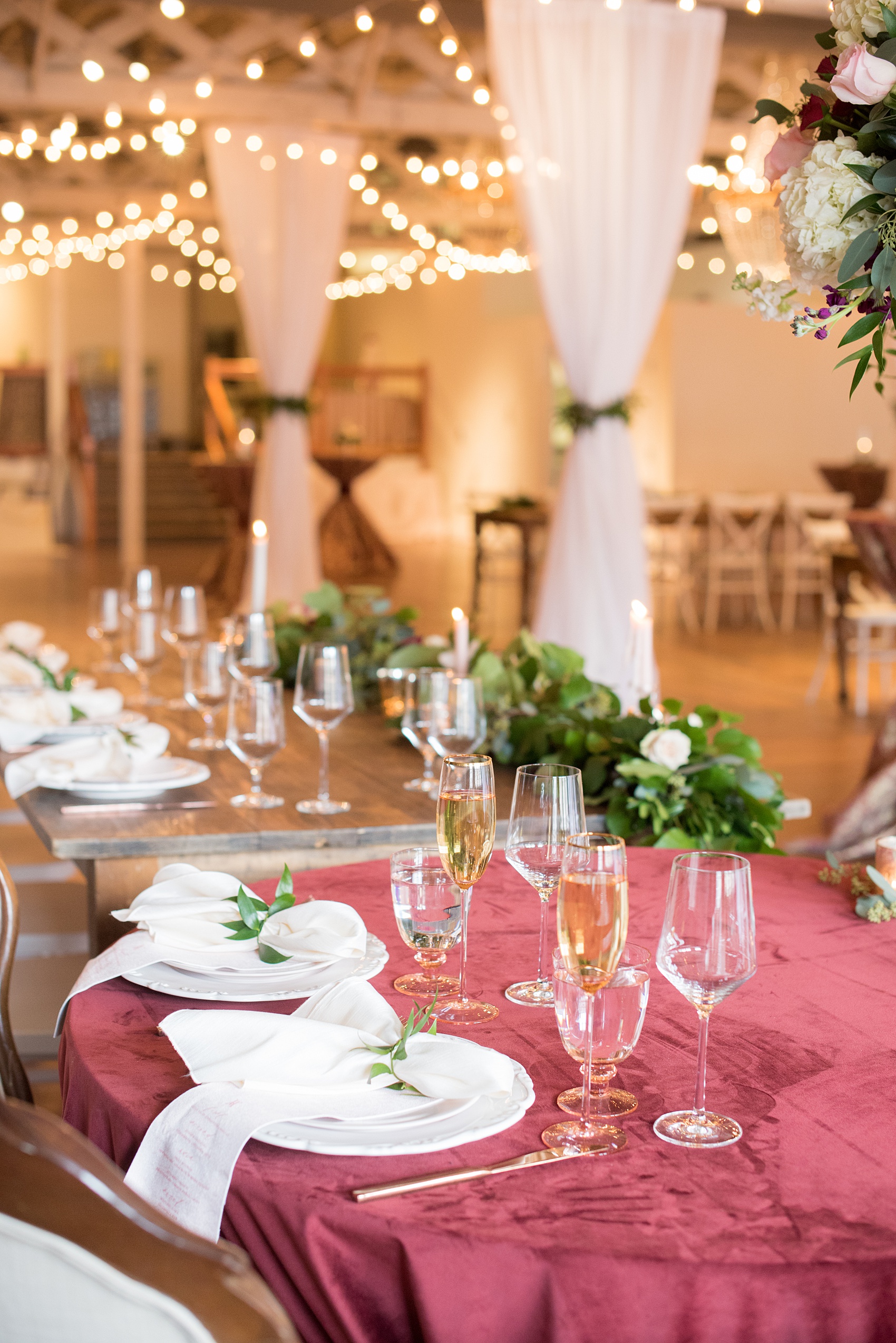 Photos from a wedding in downtown Raleigh, NC by Mikkel Paige Photography. The reception was held inside the historic venue, The Stockroom at 230. Farm tables were topped with white place settings, custom name cards with calligraphy and watercolor, and a burgundy velvet linen.