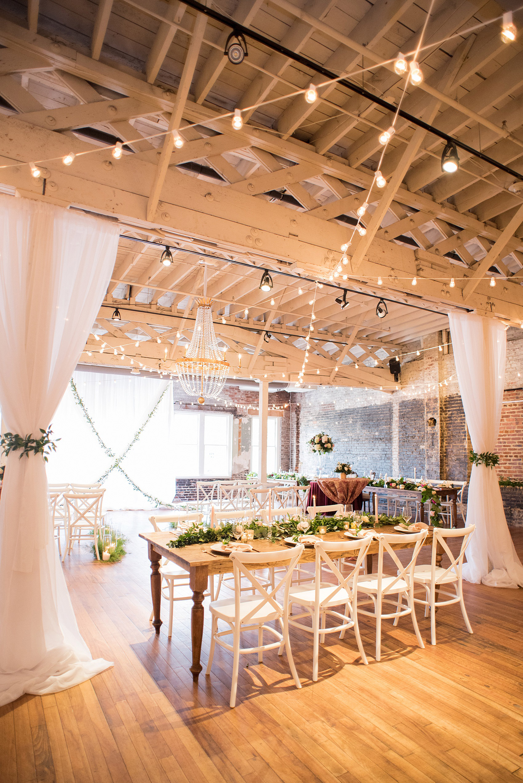 Photos from a wedding in downtown Raleigh, NC by Mikkel Paige Photography. The reception was held inside the historic venue, The Stockroom at 230. A mix of round and rectangular farm tables were dashed between white linen draping. 