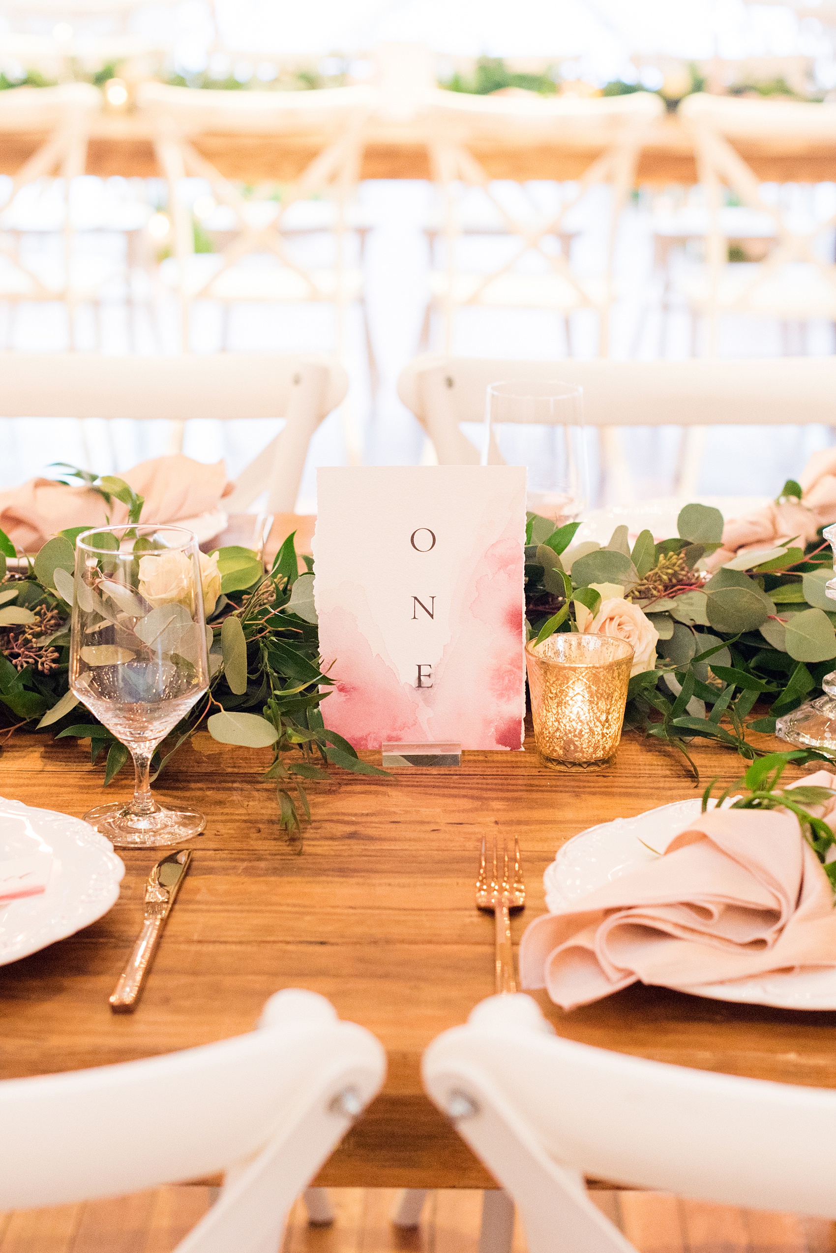 Photos from a wedding in downtown Raleigh, NC by Mikkel Paige Photography. The reception was held inside the historic venue, The Stockroom at 230. Custom table numbers were created with shades of pink and mauve watercolor by One and Only paper, placed on farm tables set with copper flatware and green garland by Tre Bella.