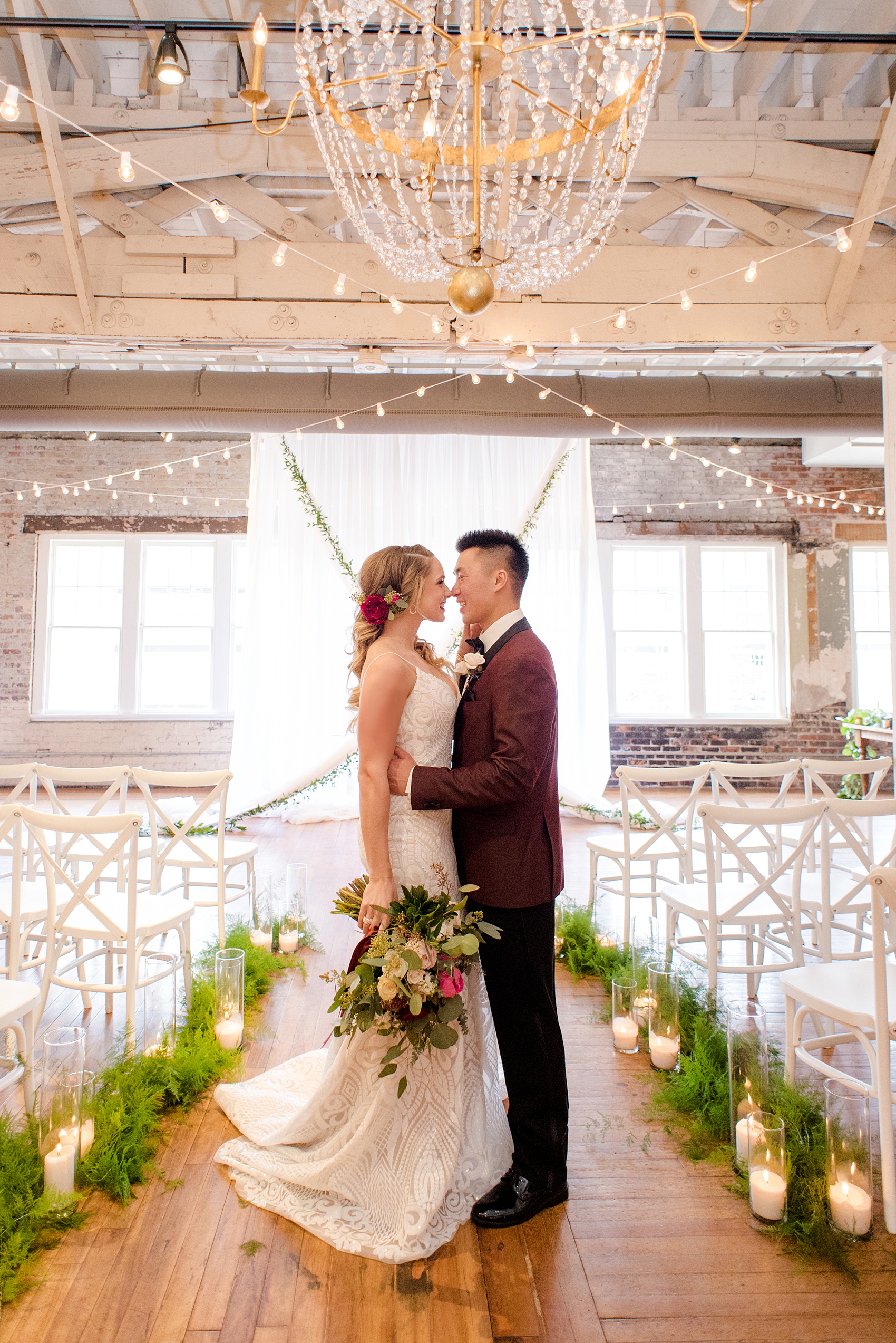 Photos from a wedding in downtown Raleigh, NC by Mikkel Paige Photography. The ceremony was held inside the historic venue, The Stockroom at 230, with white drapery and green garland hung up behind the bride and groom as they exchanged vows.