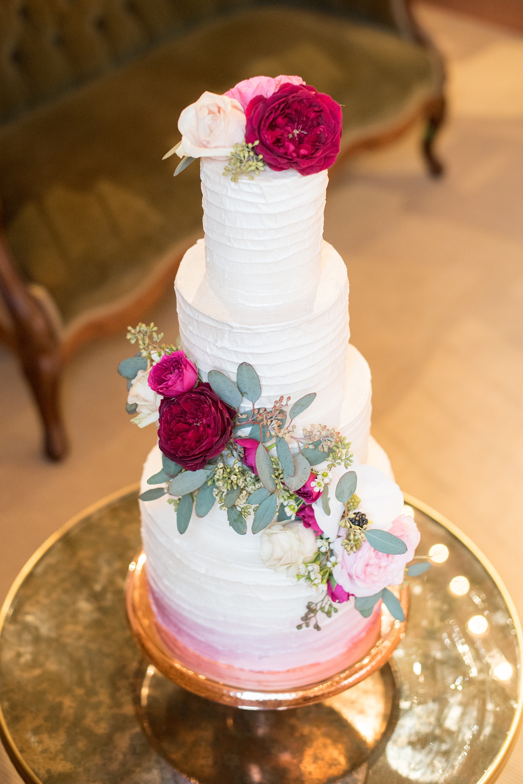 Photos from a wedding in downtown Raleigh, NC by Mikkel Paige Photography. The reception dessert options included cake and red and white macarons. The three tiered white buttercream creation was decorated with cascading fuchsia, maroon, burgundy and white flower and eucalyptus and dusted with luster powder in a pink ombre, by The Cupcake Shoppe.