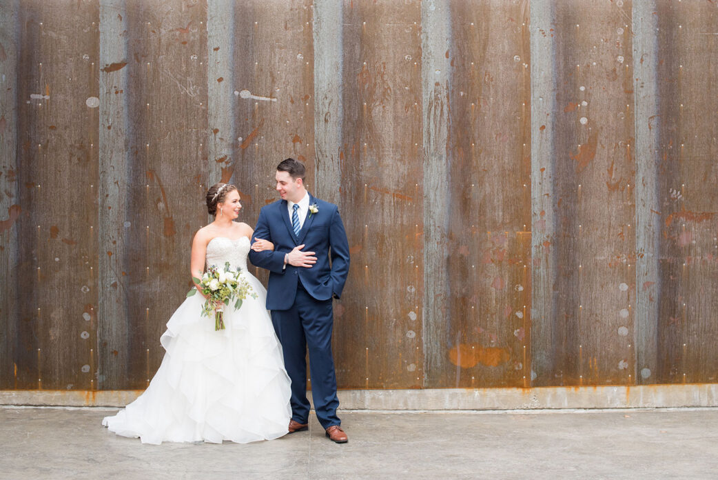 Durham wedding photos at The Cookery by Mikkel Paige Photography in North Carolina. The bride and the groom took pictures in front of a rustic, urban wall at the venue.
