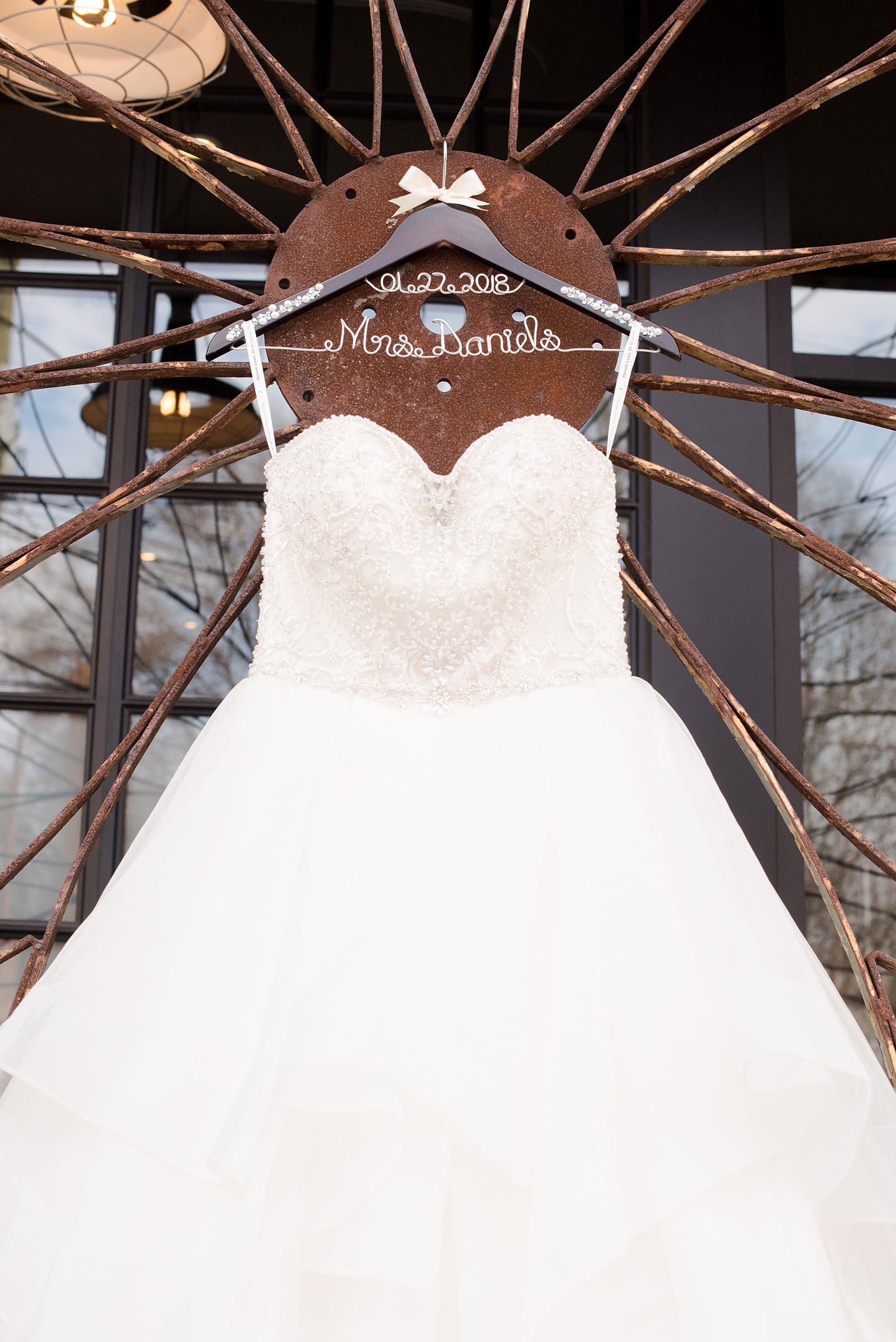 Durham wedding photos at The Cookery by Mikkel Paige Photography in North Carolina. The bride wore a strapless beaded gown, shown in a detailed picture on a rustic front gate at the venue, on a special pearl and rhinestone hanger.