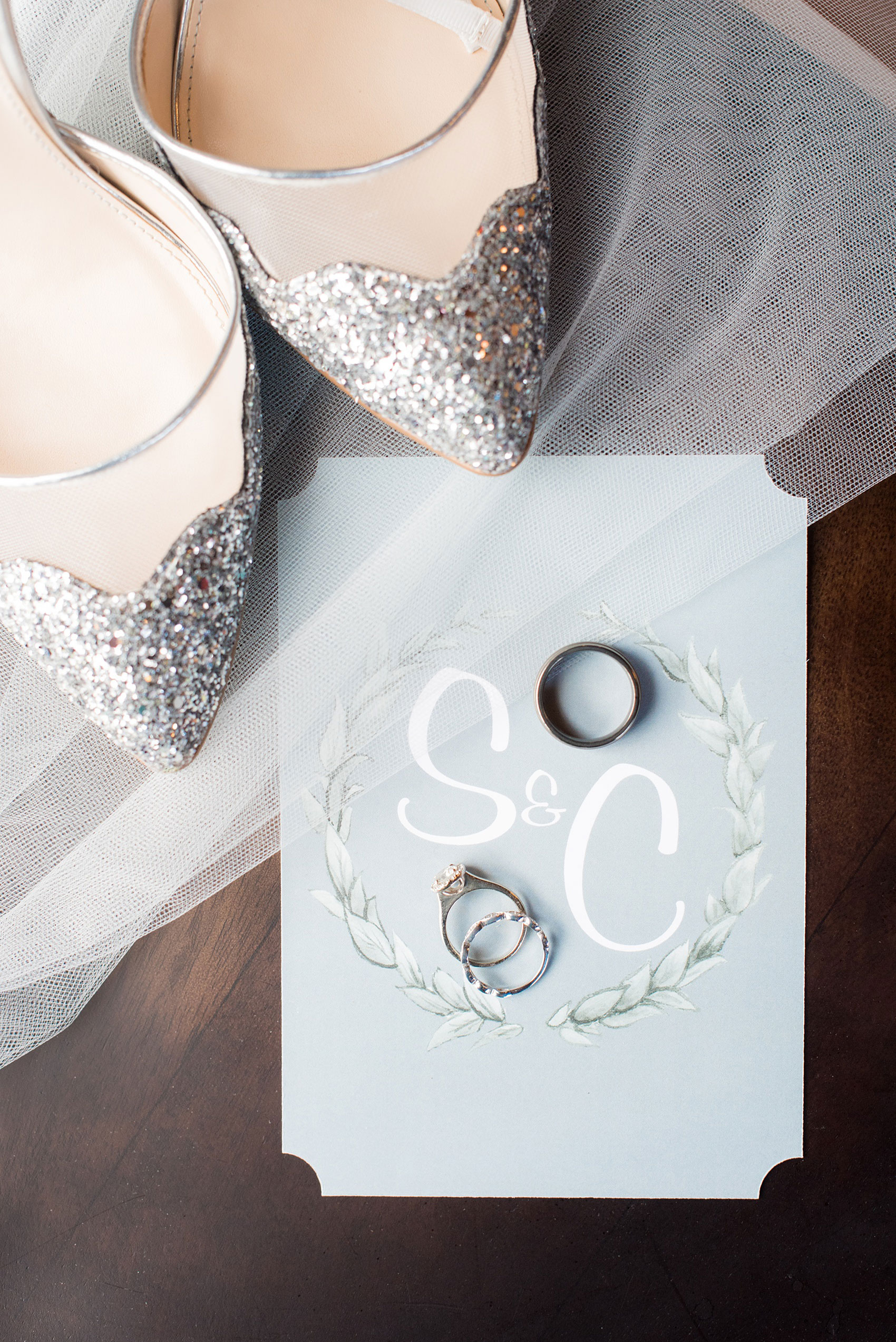 Durham wedding photos at The Cookery by Mikkel Paige Photography in North Carolina. The bride's glitter shoes, couple's rings and monogrammed back of their winter invitation are styled in this detail photo.