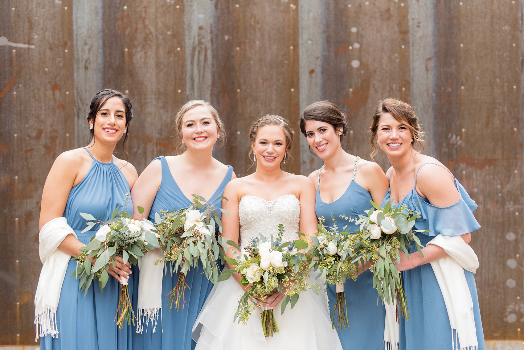 Bridesmaids Durham wedding photos at The Cookery by Mikkel Paige Photography in North Carolina. The bridal party wore different blue dresses, had white shawls for the winter wedding, and stood by the bride for this urban picture.