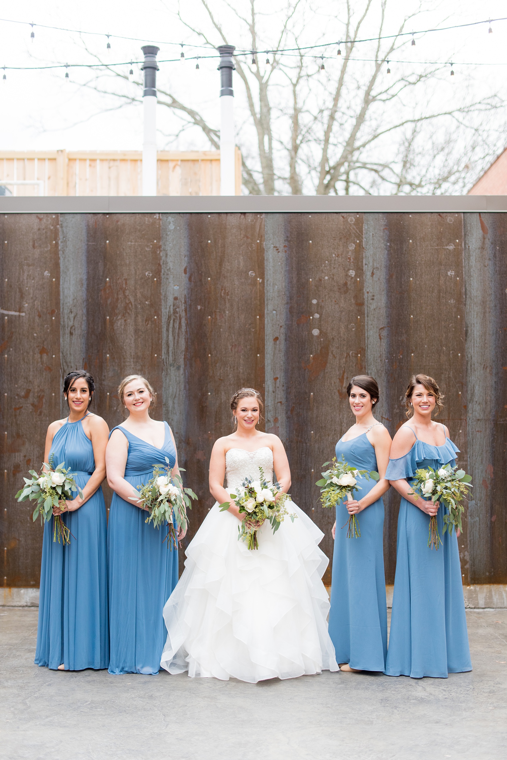 Durham wedding photos at The Cookery by Mikkel Paige Photography in North Carolina. The bridal party wore dusty cornflower blue dresses. Each gown was different and they all held a bouquet of roses and eucalyptus.