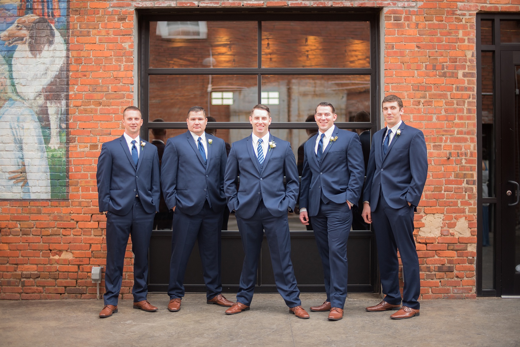 Durham wedding photos at The Cookery by Mikkel Paige Photography in North Carolina. The groomsmen wore navy blue suits with ties and brown shoes, posing for a picture in front of the brick urban outside of the venue.