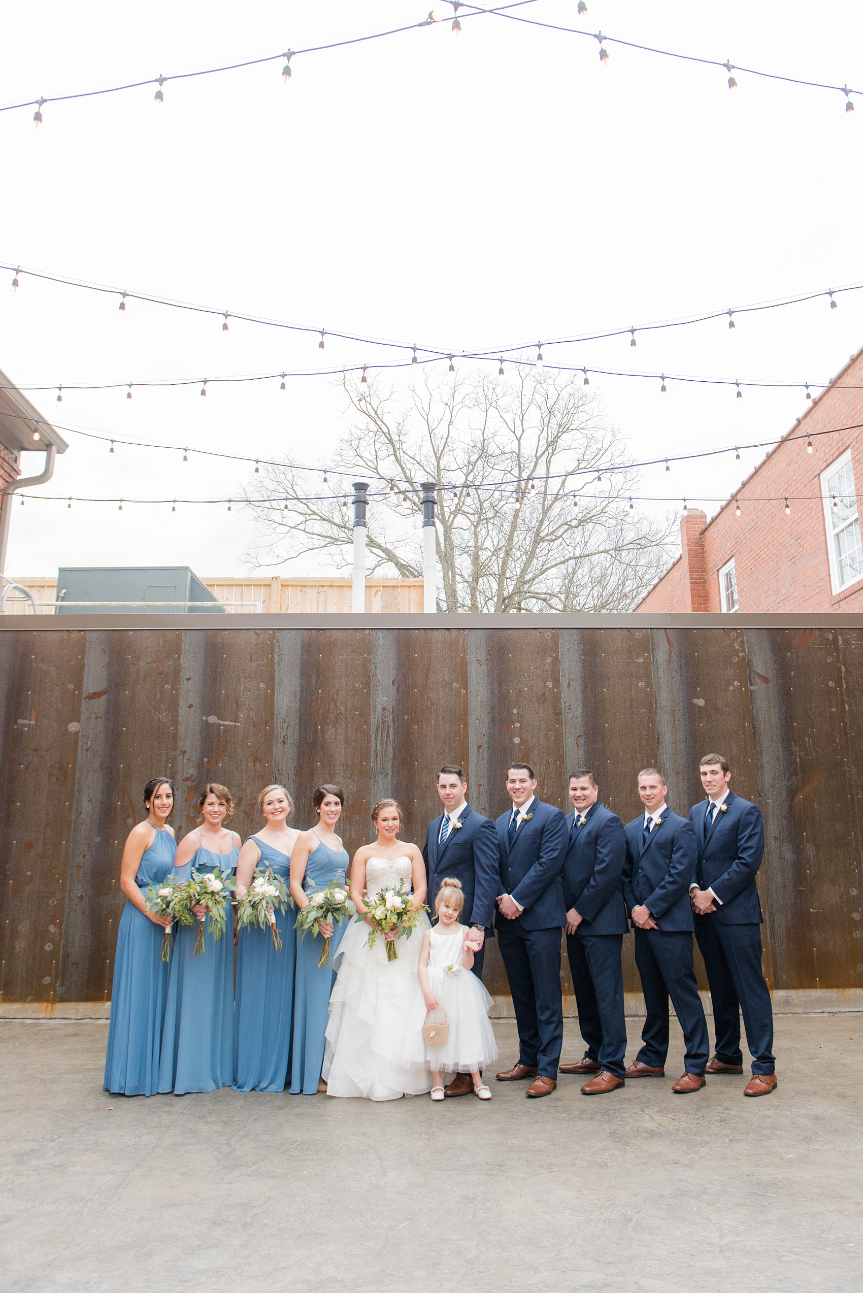 Durham wedding photos at The Cookery by Mikkel Paige Photography in North Carolina. The bridal party took pictures in front of a rustic, urban wall at the venue.