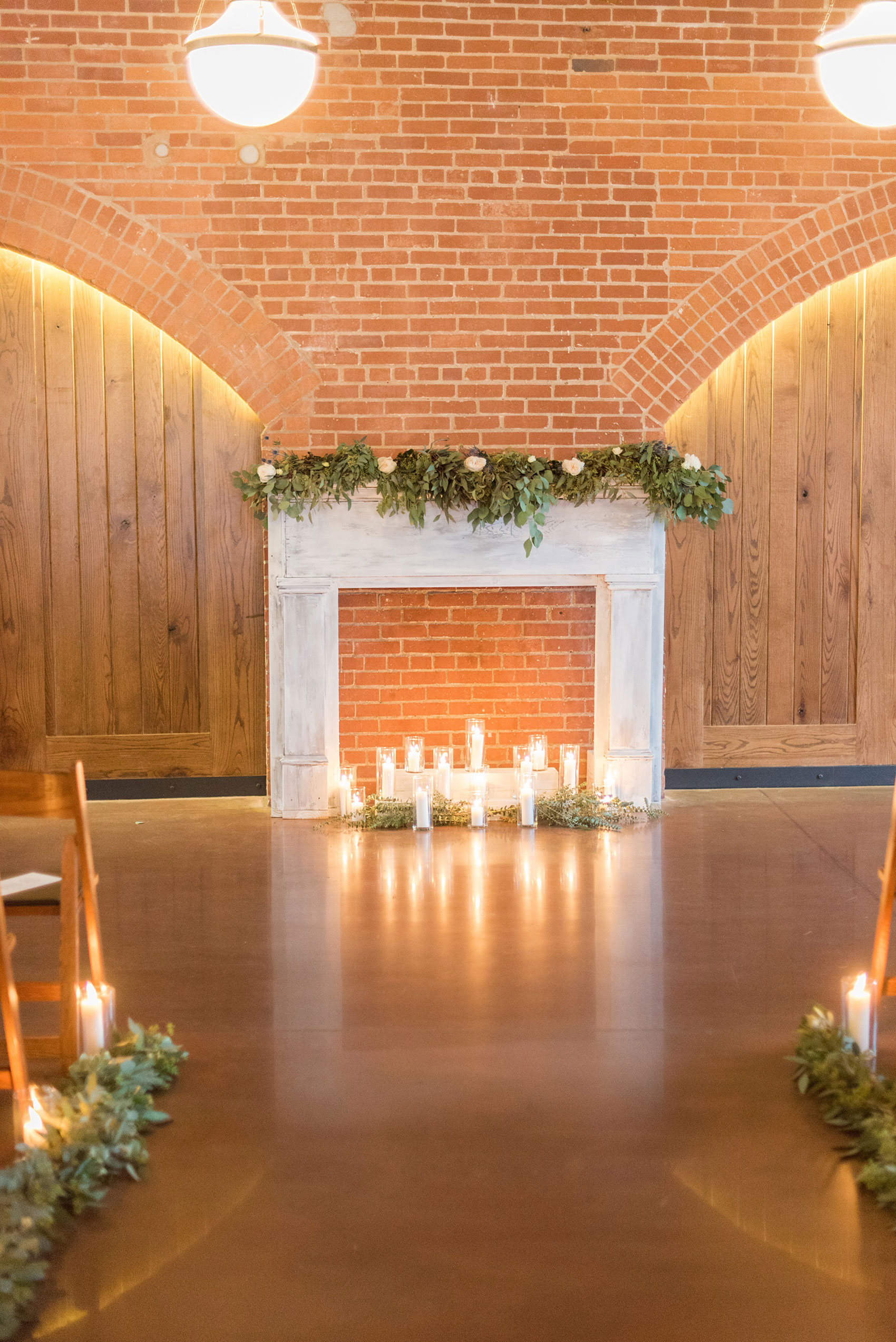 Durham wedding photos at The Cookery by Mikkel Paige Photography in North Carolina. The bride's father created a faux fireplace, decorated with lots of candlelight and green garland and white roses. It served as the indoor ceremony backdrop and eucalyptus lined the aisle.