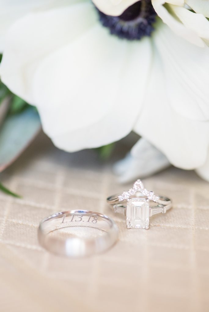 Wedding photos at Sleepy Hollow Country Club for a winter reception in January by Mikkel Paige Photography. A detail picture of their white gold wedding bands with their winter wedding date inscribed. The bride had an emerald cut diamond engagement ring and pointed band.