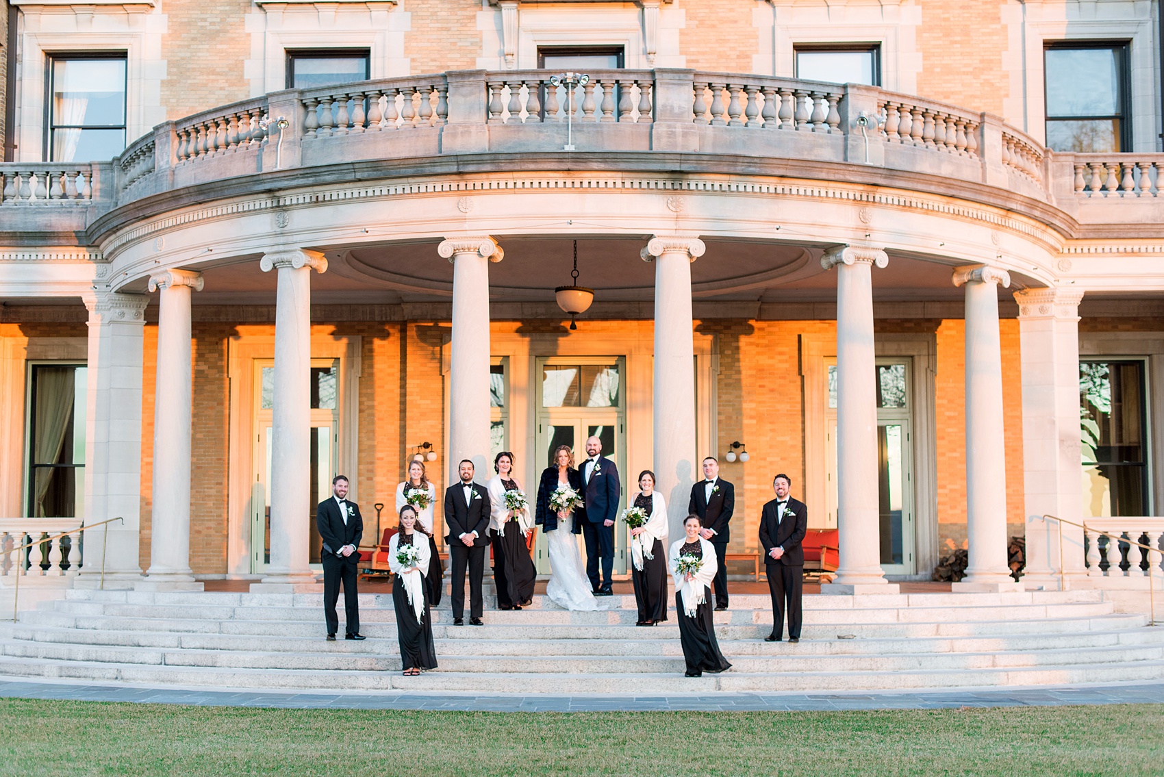 Wedding photos at Sleepy Hollow Country Club for a winter reception in January by Mikkel Paige Photography. The bridal party is pictured with white shawls, black lace gowns, and black tuxedos on the iconic stairs with columns of this New York venue.