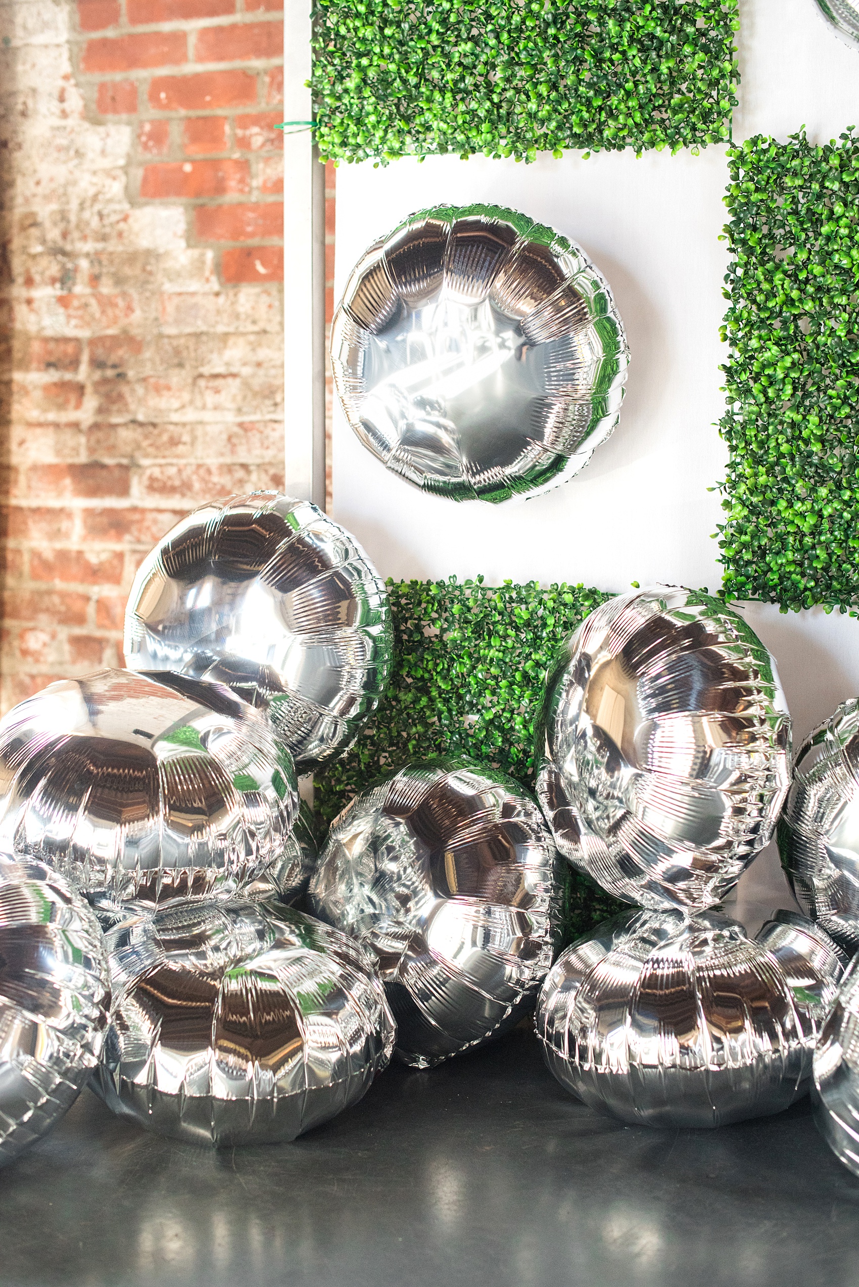 Mikkel Paige Photography photos of a wedding at the Green Building in Brooklyn, New York. This same sex, gay marriage styled shoot was created by Color Pop Events. This picture of the ceremony background, altar setup shows silver mylar balloons and green square boxwood patches.