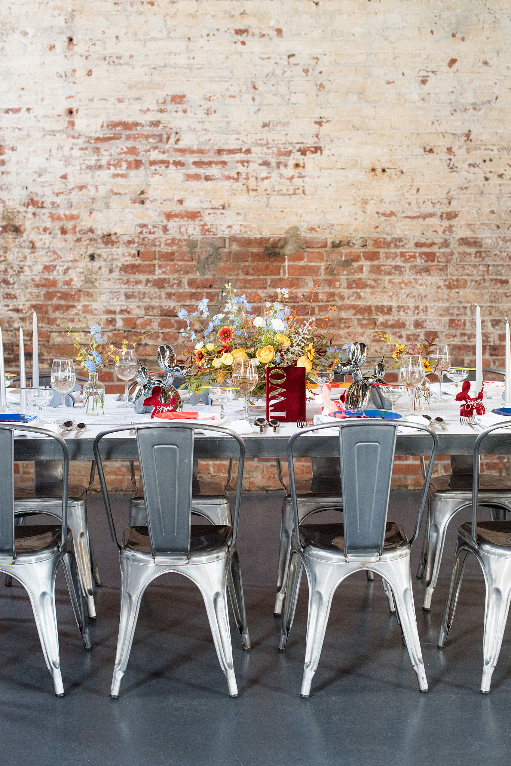 Mikkel Paige Photography photos of a wedding at the Green Building in Brooklyn, New York. This same sex, gay marriage styled shoot was created by Color Pop Events. This pictures shows the urban dinner table was styled by Taylor and Hov, inspired by Jeff Koons and neo pop art. Flower centerpieces are by Abby Tabak Studio.