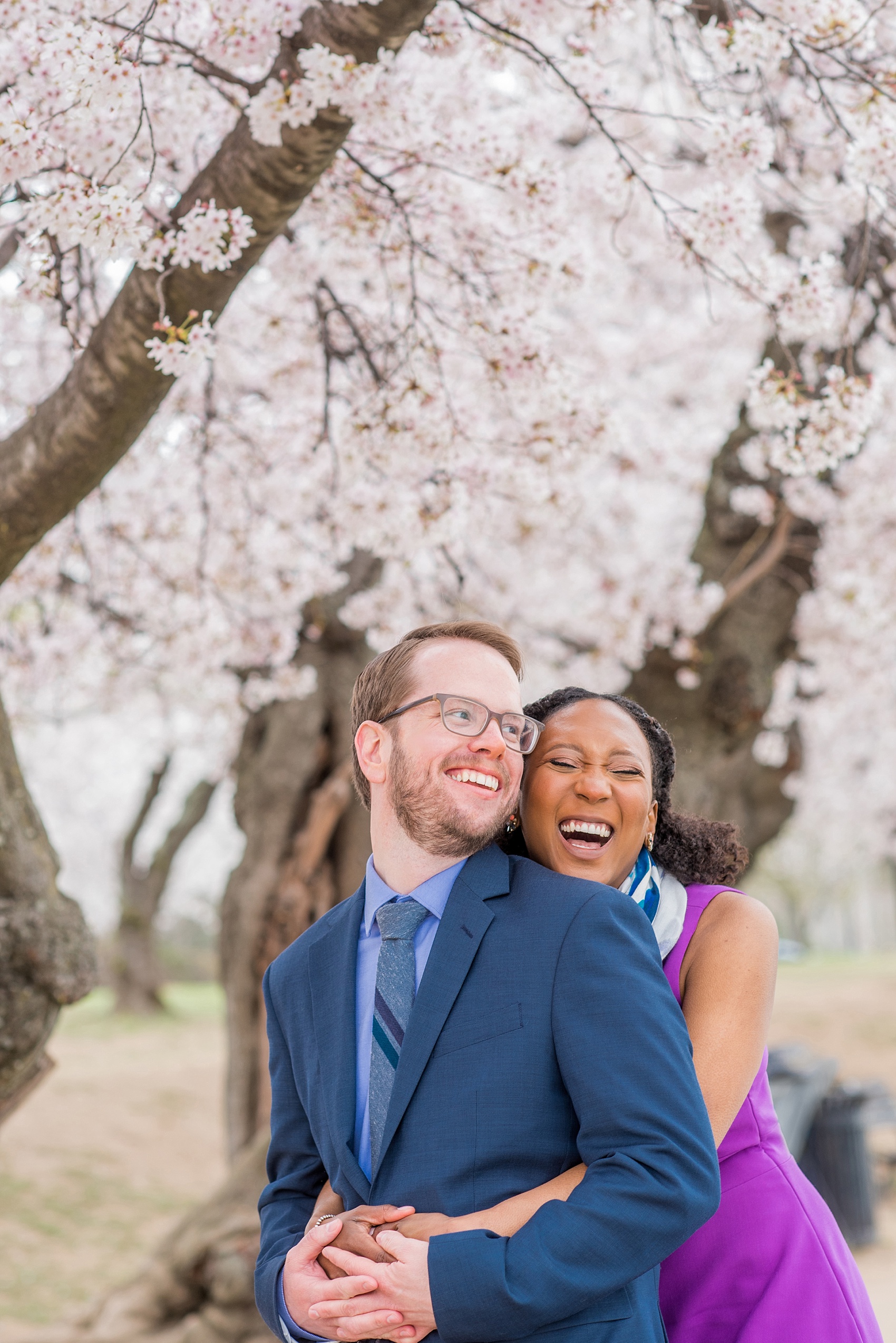 DC Cherry Blossoms Engagement Photos by Mikkel Paige Photography. Spring flowers at the Martin Luther King Jr. memorial with the Washington Monument in the background, at the nation's Capitol with an interracial couple in colorful outfits. #DCCherryBlossoms #CherryBlossoms #EngagementPhotos #SpringEngagementPhotos #CherryBlossomsEngagementPhotos