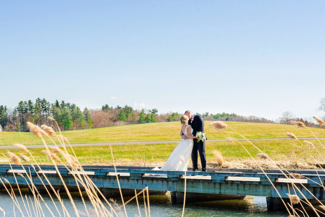 Saratoga Springs destination wedding photos by Mikkel Paige Photography. The bride and groom shared a kiss on the bridge surrounded by spring greenery for their reception held at Saratoga National Golf Club venue. #SaratogaSpringsNY #SaratogaSprings #mikkelpaige #NYwedding #destinationwedding