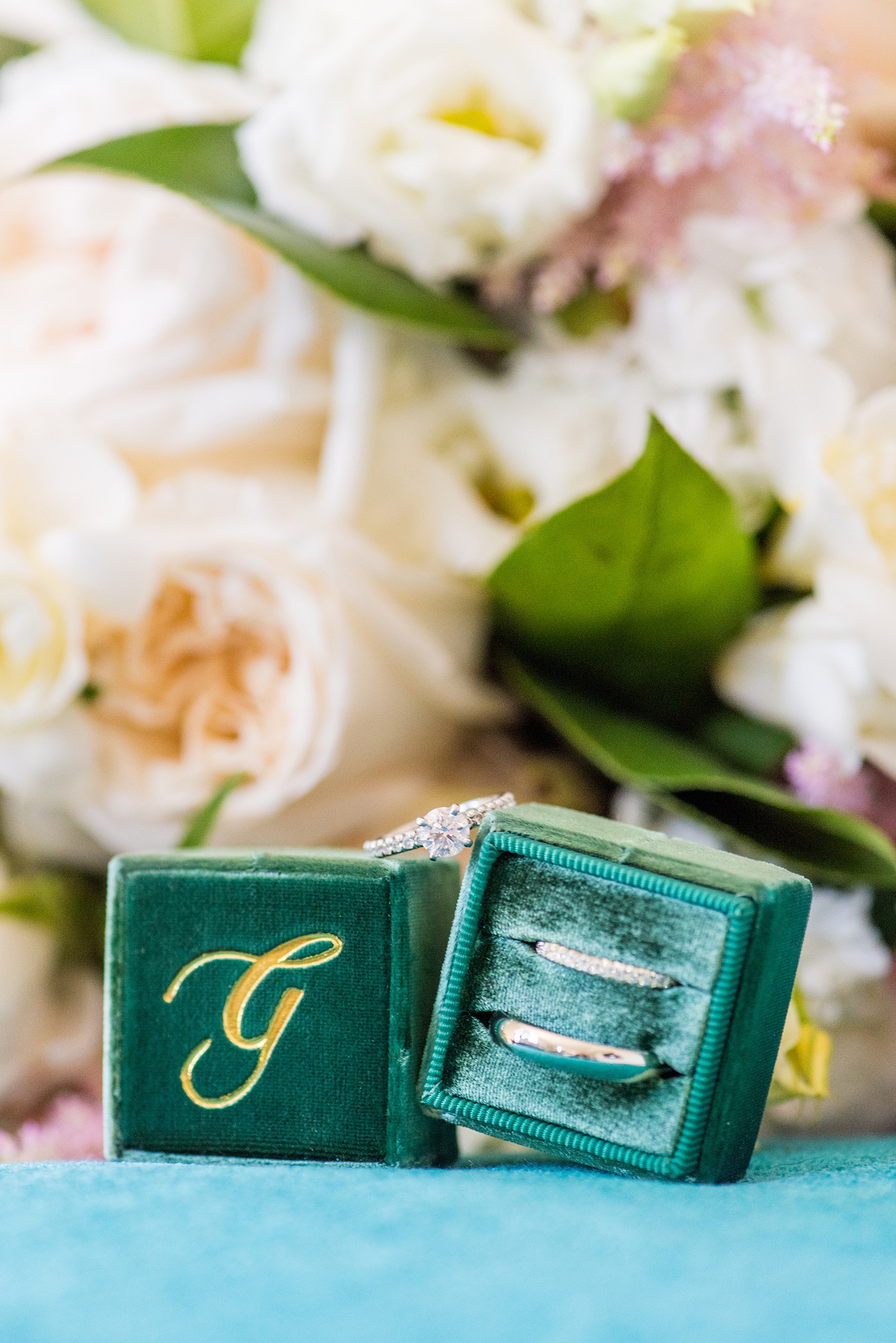 Saratoga Springs destination wedding photos by Mikkel Paige Photography. This detail picture shows the bride and groom's white gold wedding bands and diamond engagement ring with a "G" monogram green velvet Mrs. Box and her white and pink bouquet. #SaratogaSpringsNY #SaratogaSprings #mikkelpaige #NYwedding #destinationwedding #TheMrsBox #EngagementRing #RingBox