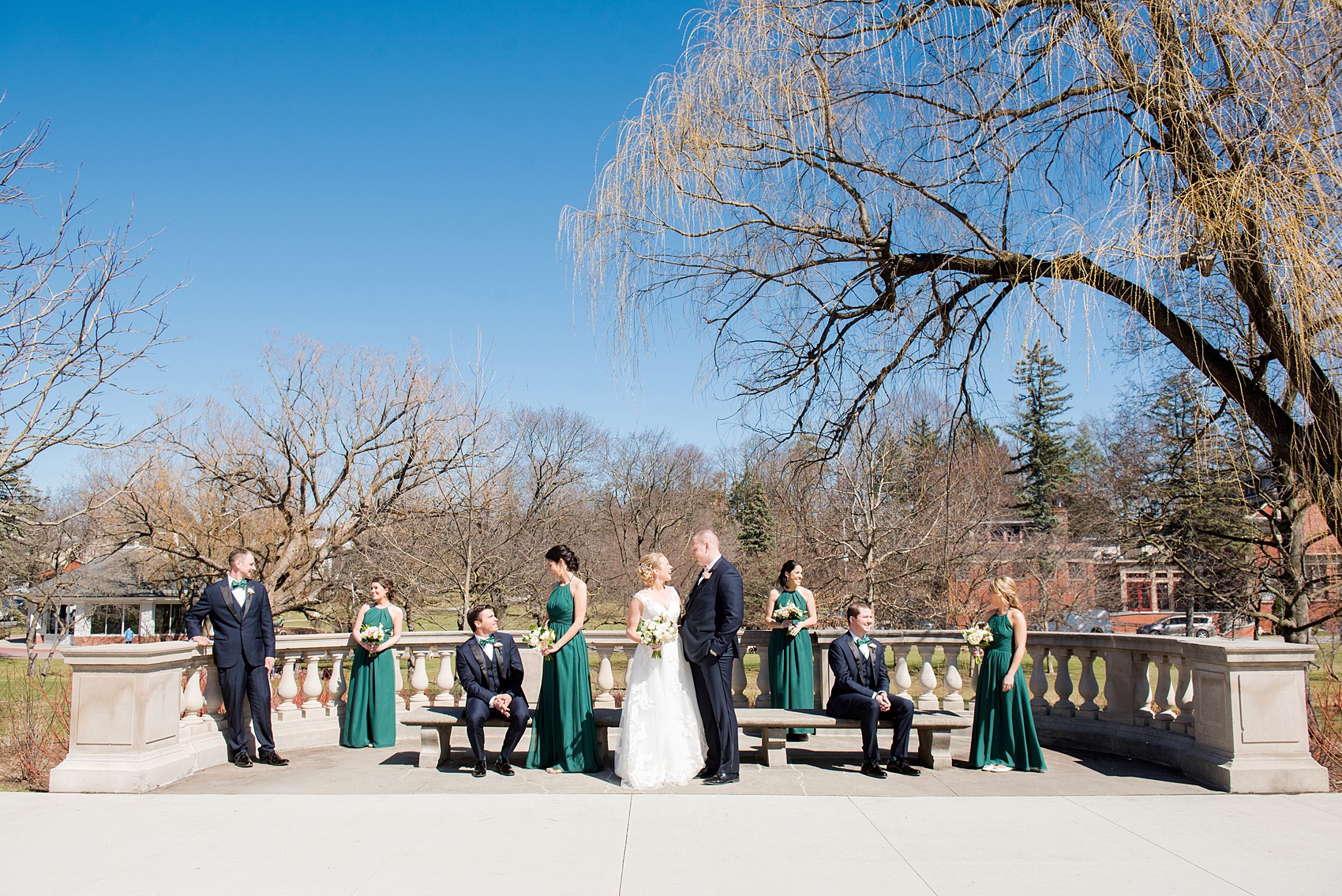 Saratoga Springs destination wedding photos by Mikkel Paige Photography. This picture shows the bride and groom with their wedding party (bridal party) in navy blue suits with a black lapel, and long dark green gowns for the bridesmaids. #SaratogaSpringsNY #SaratogaSprings #mikkelpaige #NYwedding #destinationwedding #greenweddinginspiration #greenwedding #greenandgoldwedding #greenbridesmaids #vogueweddingphoto #uniqueweddingphoto #creativeweddingphotos