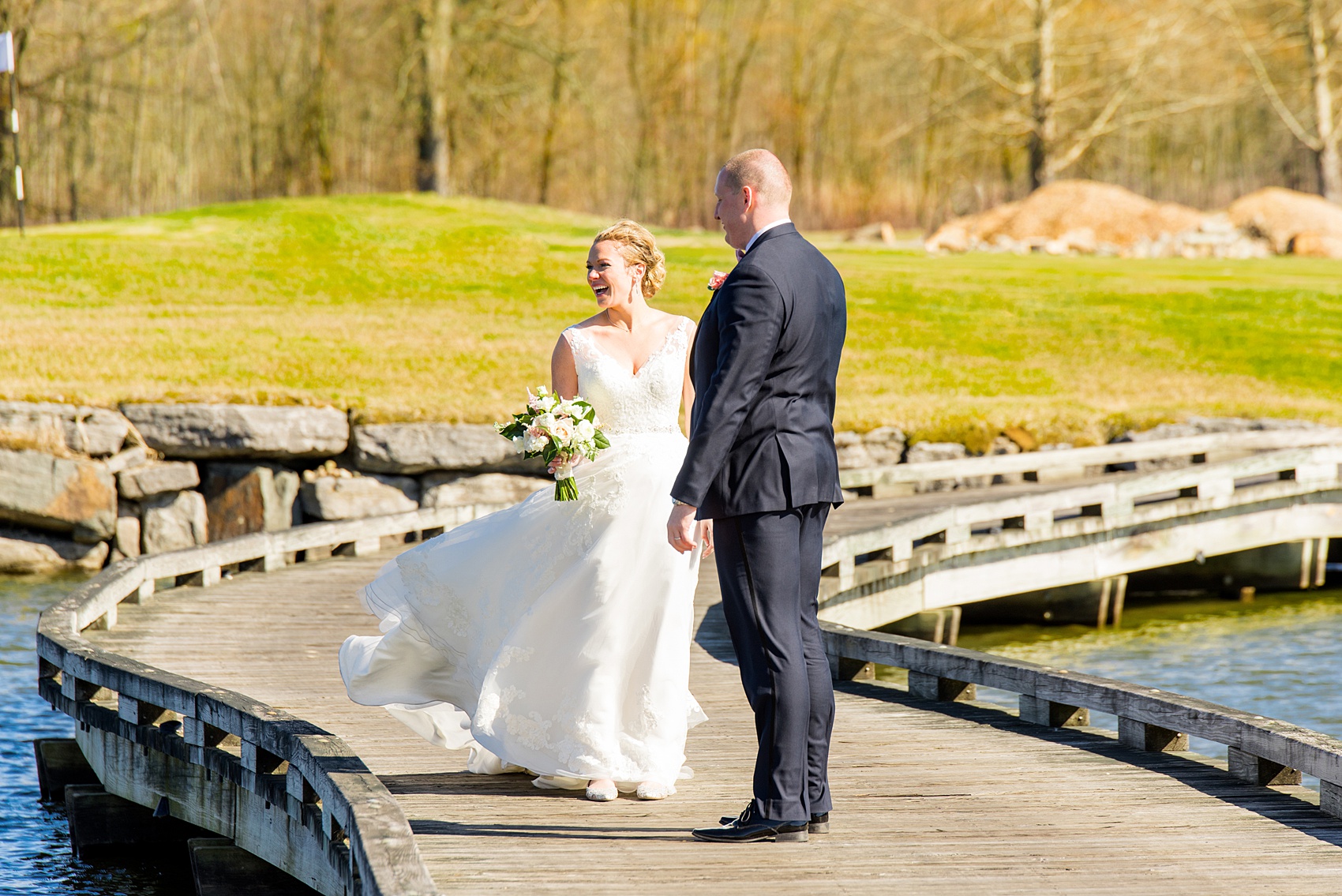 Saratoga Springs destination wedding photos by Mikkel Paige Photography. The bride and groom share a laughing moment on the bridge surrounded by spring greenery for their reception held at Saratoga National Golf Club venue. #SaratogaSpringsNY #SaratogaSprings #mikkelpaige #NYwedding #destinationwedding