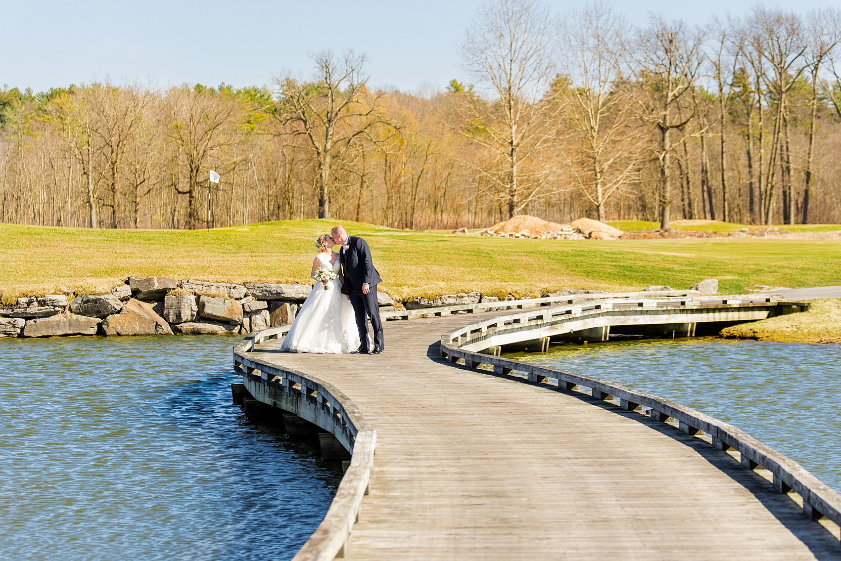 Saratoga Springs destination wedding photos by Mikkel Paige Photography. The bride and groom share a kiss on the bridge surrounded by spring greenery for their reception held at Saratoga National Golf Club venue. #SaratogaSpringsNY #SaratogaSprings #mikkelpaige #NYwedding #destinationwedding