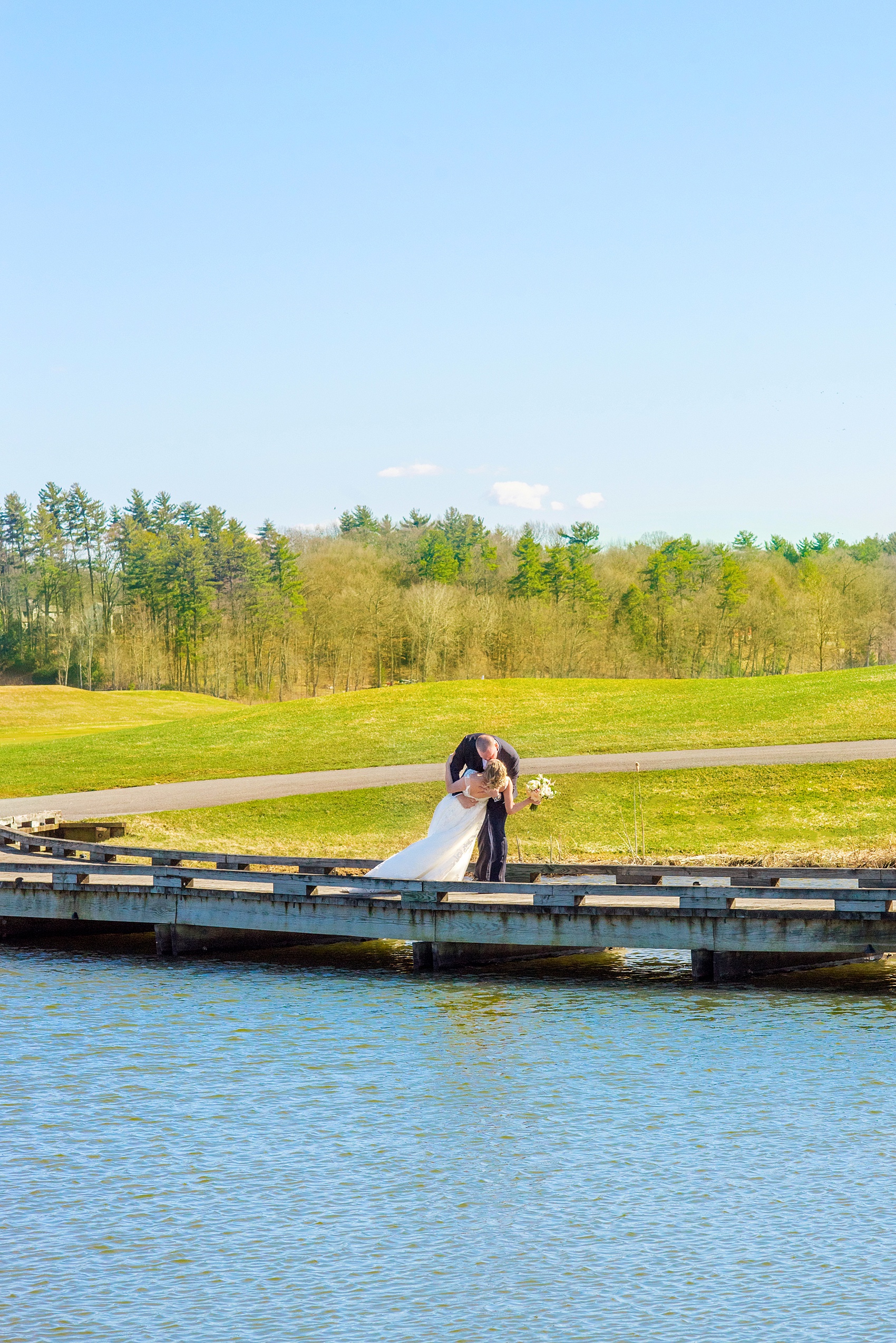 Saratoga Springs destination wedding photos by Mikkel Paige Photography. The bride and groom share a kiss on the bridge surrounded by spring greenery for their reception held at Saratoga National Golf Club venue. #SaratogaSpringsNY #SaratogaSprings #mikkelpaige #NYwedding #destinationwedding 