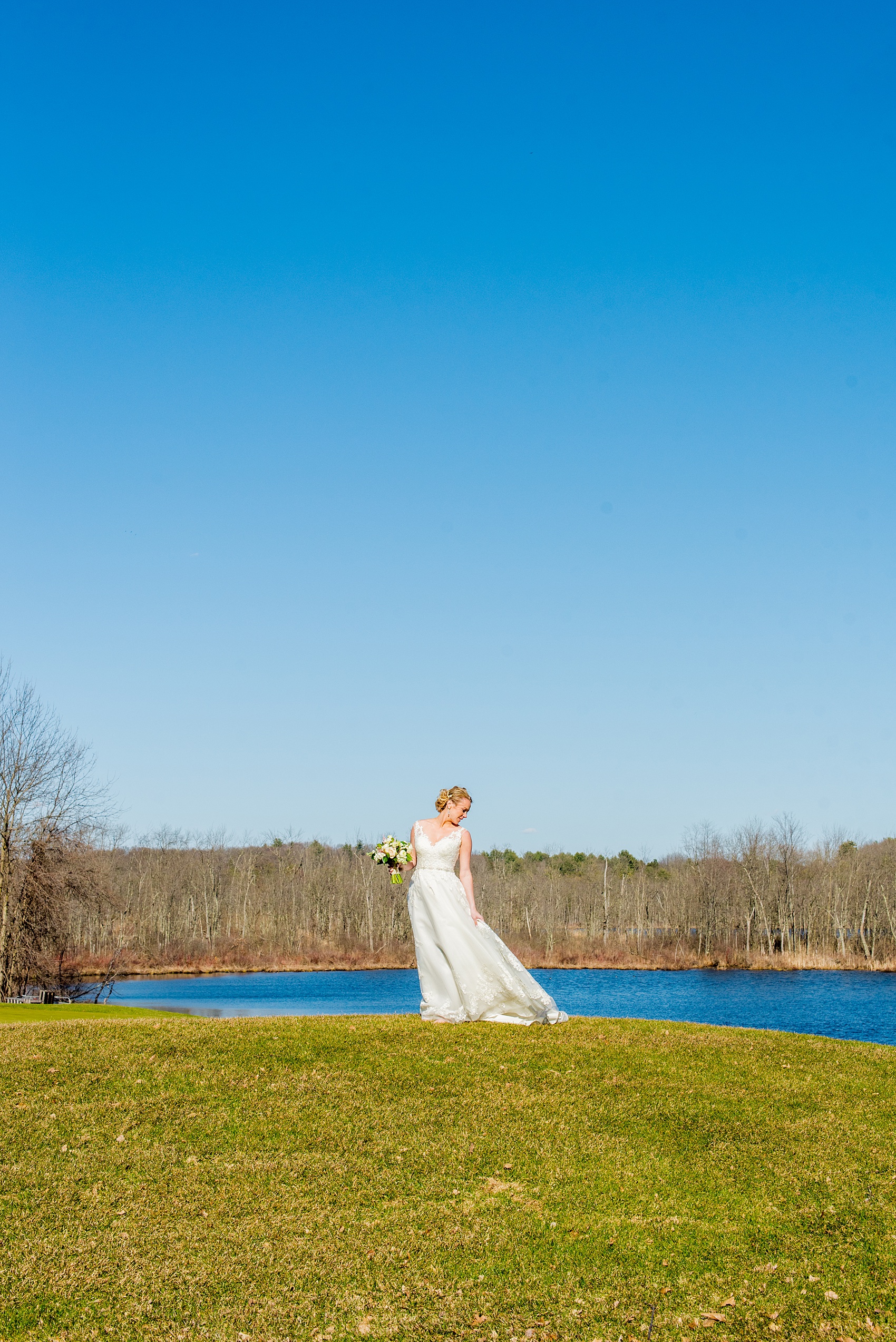 Saratoga Springs destination wedding photos by Mikkel Paige Photography. This iconic photo shows the bride's tulle skirt blowing in the wind against a blue spring sky on the venue's property at Saratoga National Golf Club for her April wedding. #SaratogaSpringsNY #SaratogaSprings #mikkelpaige #NYwedding #destinationwedding 