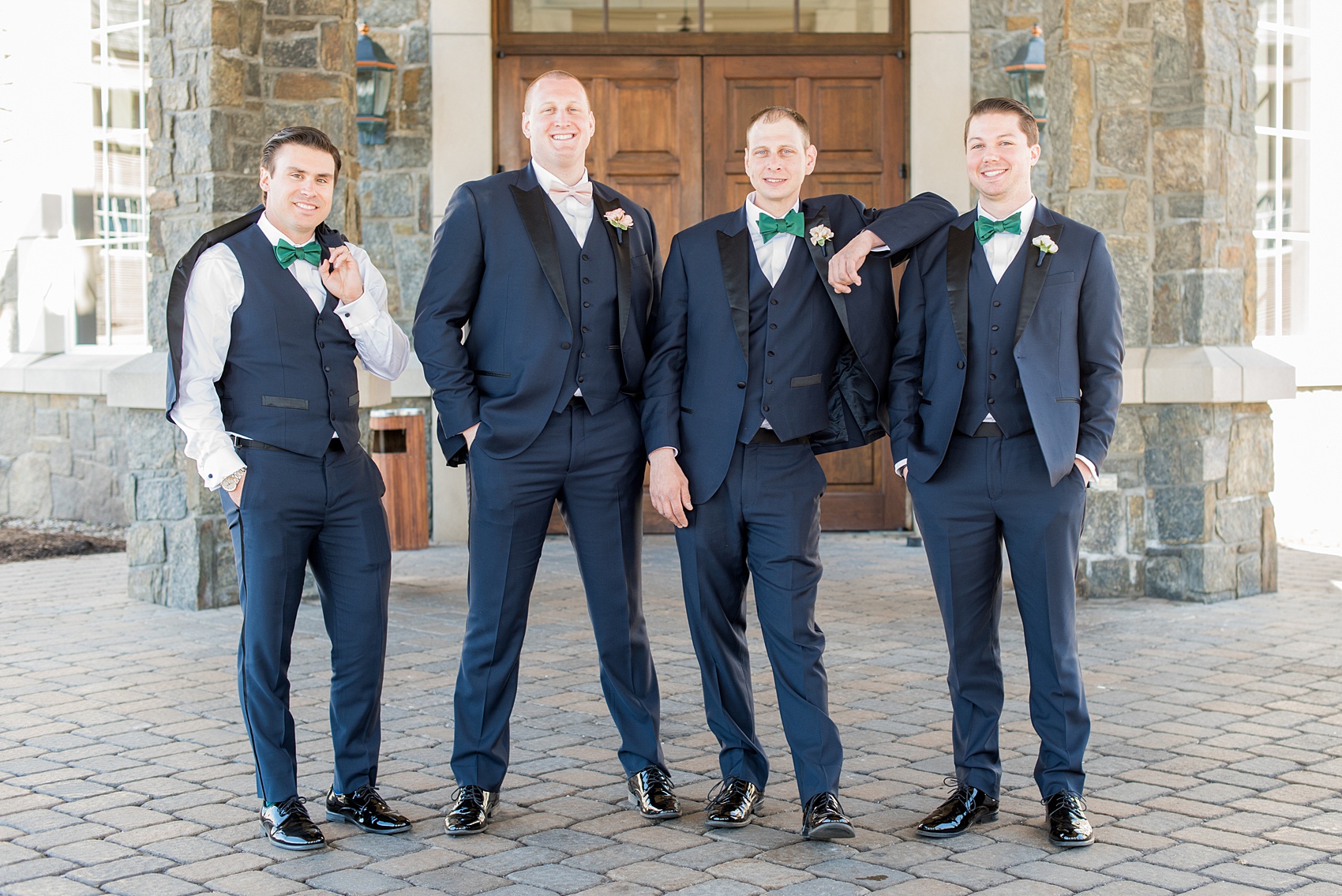 Saratoga Springs destination wedding photos by Mikkel Paige Photography. This picture shows the groom and groomsmen in navy blue tuxedos with black lapels, green bow ties (blush pink for the groom) and white spray rose boutonnieres tied with ribbon. The spring event was held at Saratoga National Golf Club venue. #SaratogaSpringsNY #SaratogaSprings #mikkelpaige #NYwedding #destinationwedding #navyblueandblacktuxedo