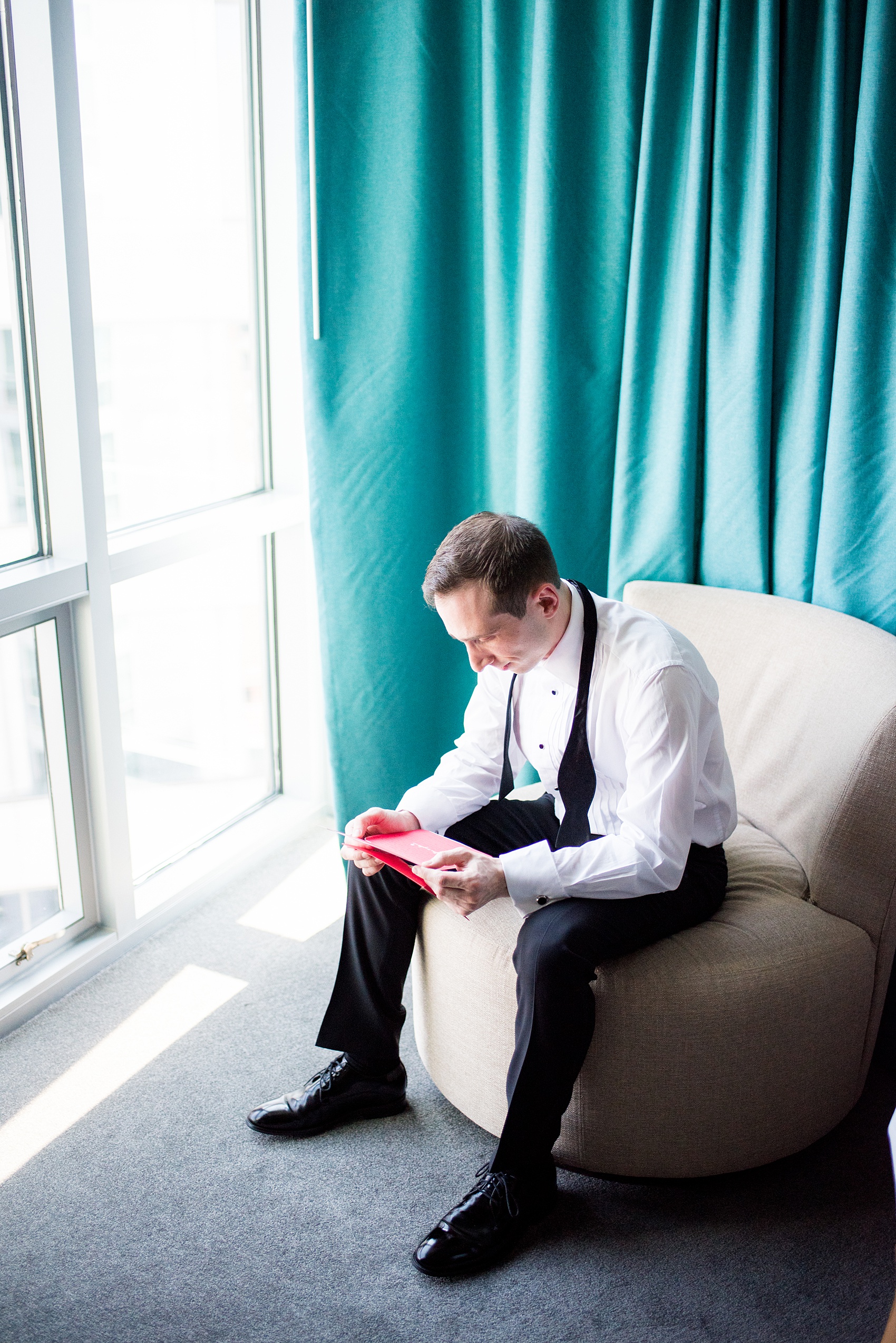 W Hoboken wedding photos by Mikkel Paige Photography. Pictures in this well known New Jersey venue with a view of the Manhattan skyline. Image of the groom during the start of the afternoon, getting ready at the colorful teal Starwood hotel, reading a card from his bride. #mikkelpaige #HobokenWedding #NewJerseyPhotographer #NewYorkCityPhotographer #NYCweddingphotographer #brideandgroomphotos #redpeonies #romanticwedding #springwedding #CityWedding