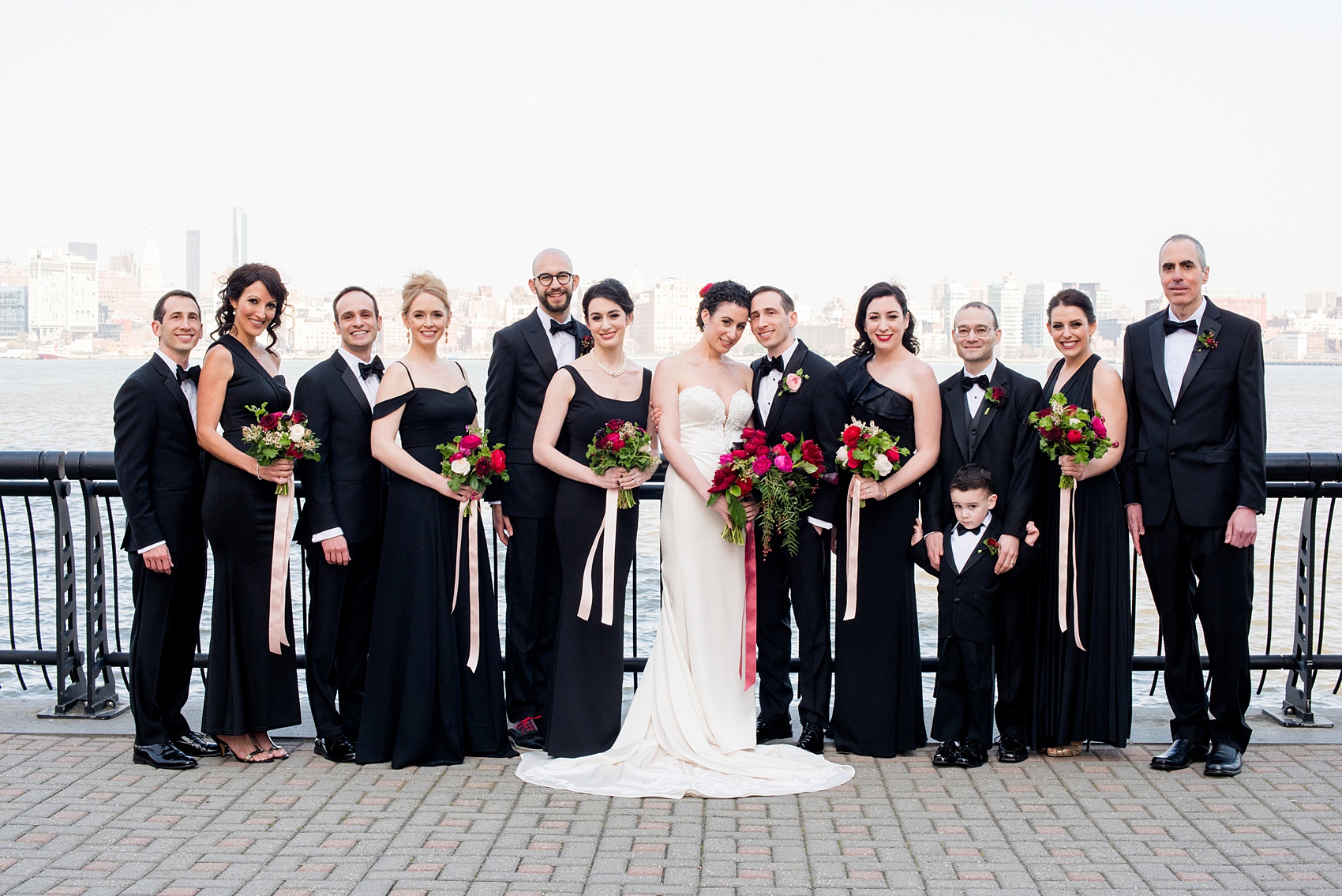 W Hoboken wedding photos at this New Jersey hotel overlooking the NYC skyline. Photos by Mikkel Paige Photography of the bridal party in black gowns carrying romantic bouquets in red and pink and groomsmen in black tuxedos. #mikkelpaige #HobokenWedding #NewJerseyPhotographer #NewYorkCityPhotographer #NYCweddingphotographer #brideandgroomphotos #redpeonies #romanticwedding #springwedding #CityWedding