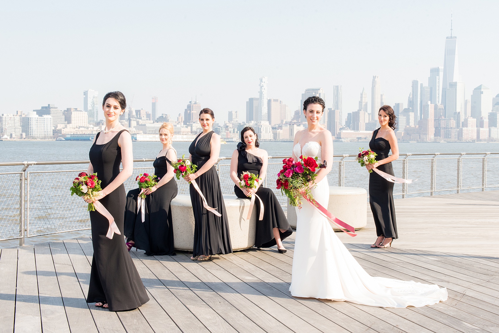 W Hoboken wedding photos at this New Jersey hotel overlooking the NYC skyline. Vogue like photo by Mikkel Paige Photography of the bridal party in black gowns carrying romantic bouquets in red and pink and long ribbons blowing in the breeze. #mikkelpaige #HobokenWedding #NewJerseyPhotographer #NewYorkCityPhotographer #NYCweddingphotographer #brideandgroomphotos #redpeonies #romanticwedding #springwedding #CityWedding