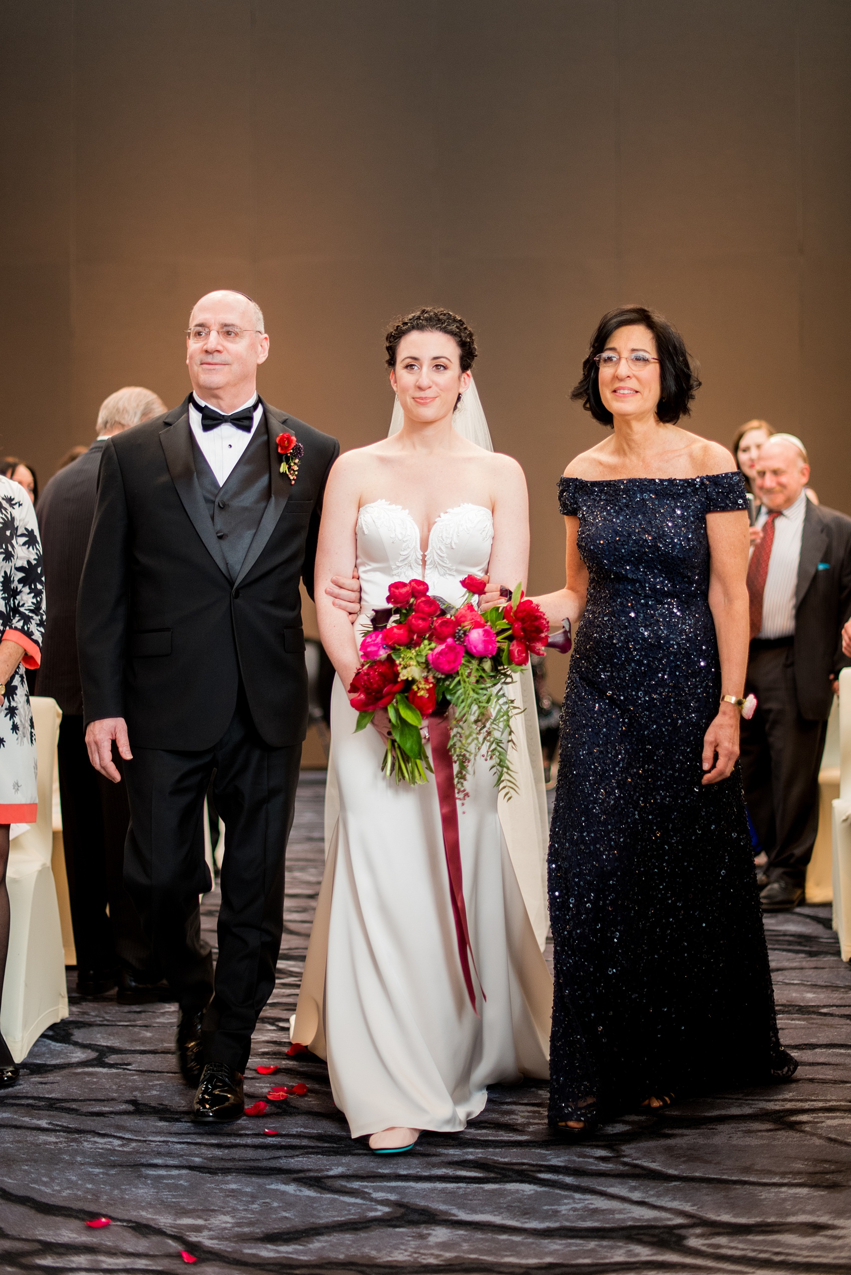 W Hoboken wedding photos at a New Jersey venue overlooking the Manhattan skyline. Photos by Mikkel Paige Photography of the indoor ceremony with the bride's mother and father walking her down the aisle for a traditional Jewish ceremony. #mikkelpaige #HobokenWedding #NewJerseyPhotographer #NewYorkCityPhotographer #NYCweddingphotographer #brideandgroomphotos #redpeonies #romanticwedding #springwedding #CityWedding #JewishWedding #Chuppah