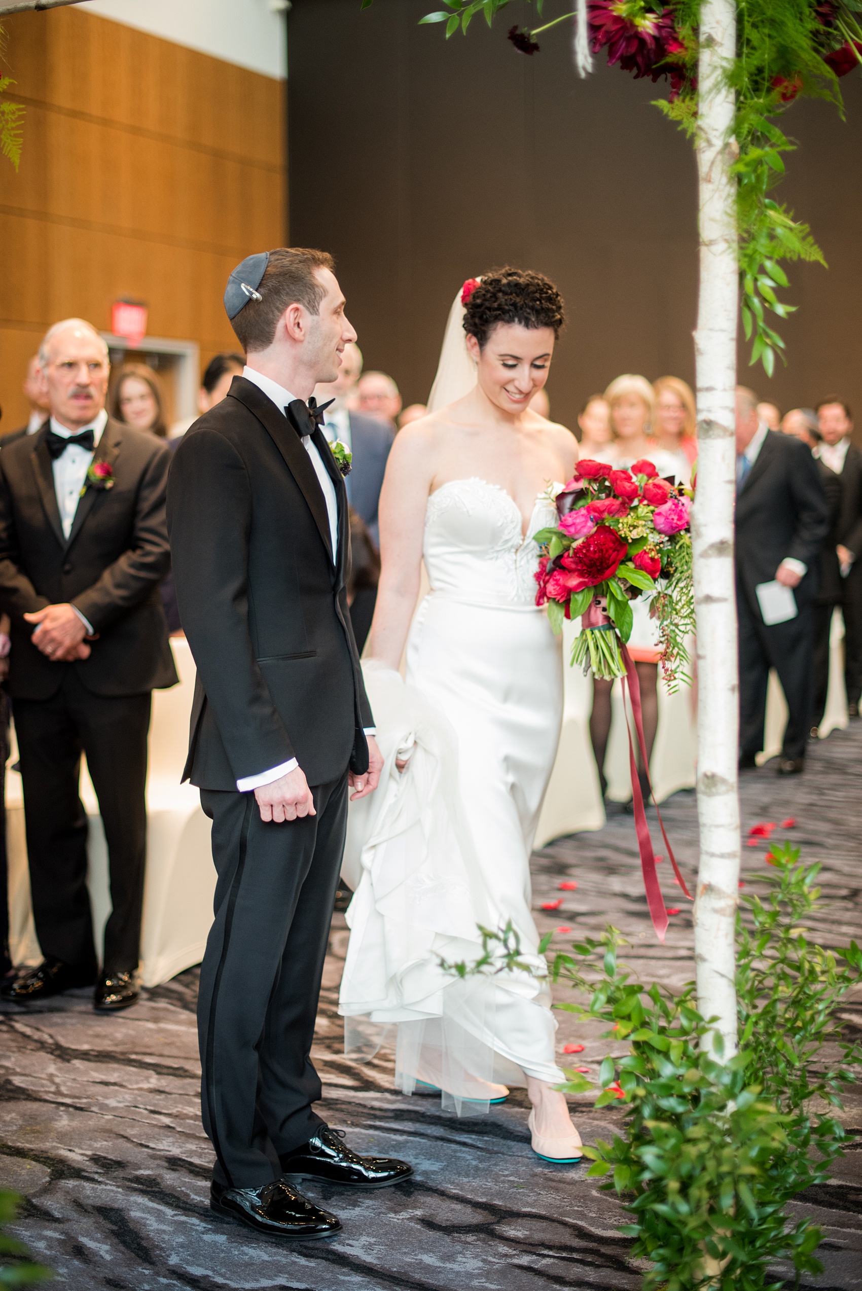 W Hoboken wedding photos at this New Jersey venue overlooking the NYC skyline. Photos by Mikkel Paige Photography of the indoor ceremony with a birch branch chuppah. Sachi Rose Design decorated it with red, pink, fuchsia and burgundy flowers. #mikkelpaige #HobokenWedding #NewJerseyPhotographer #NewYorkCityPhotographer #NYCweddingphotographer #brideandgroomphotos #redpeonies #romanticwedding #springwedding #CityWedding #JewishWedding #Chuppah