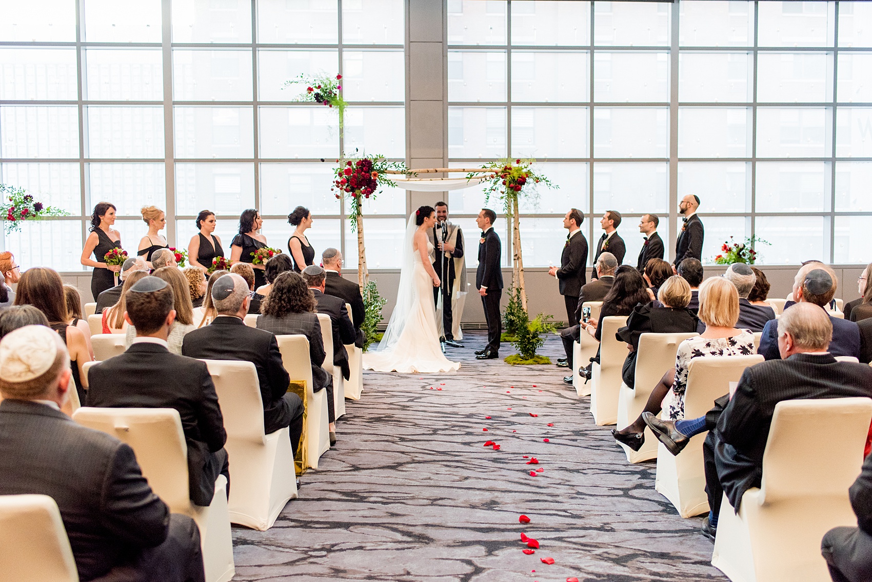 W Hoboken wedding photos at this New Jersey venue overlooking the NYC skyline. Photos by Mikkel Paige Photography of the indoor ceremony with a birch branch chuppah. Sachi Rose Design decorated it with red, pink, fuchsia and burgundy flowers. #mikkelpaige #HobokenWedding #NewJerseyPhotographer #NewYorkCityPhotographer #NYCweddingphotographer #brideandgroomphotos #redpeonies #romanticwedding #springwedding #CityWedding #JewishWedding #Chuppah