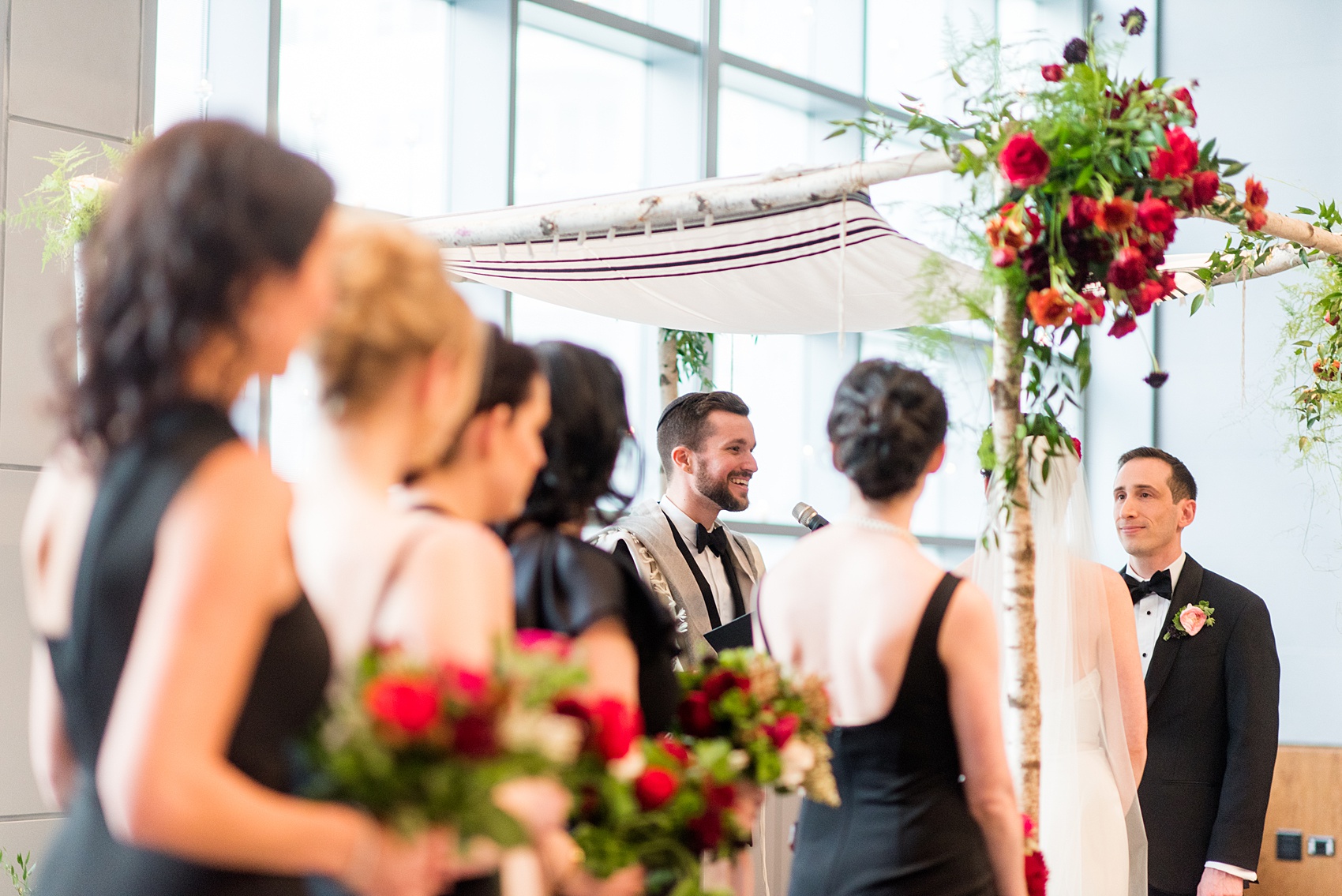 W Hoboken wedding photos at this New Jersey venue overlooking the NYC skyline. Photos by Mikkel Paige Photography of the indoor ceremony with a birch branch chuppah. Sachi Rose Design decorated it with red, pink, fuchsia and burgundy flowers. #mikkelpaige #HobokenWedding #NewJerseyPhotographer #NewYorkCityPhotographer #NYCweddingphotographer #brideandgroomphotos #redpeonies #romanticwedding #springwedding #CityWedding #JewishWedding #Chuppah