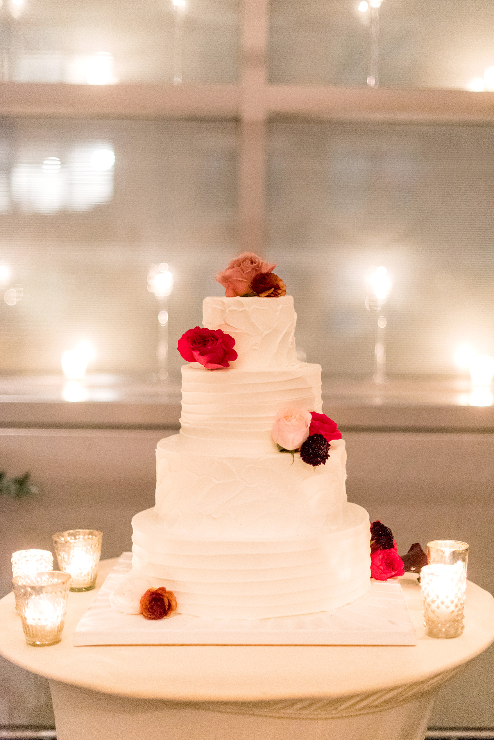 W Hoboken wedding photos at this New Jersey venue overlooking the NYC skyline. Photos by Mikkel Paige Photography of the reception white tiered buttercream cake decorated with fresh pink, red and burgundy flowers. #mikkelpaige #HobokenWedding #NewJerseyPhotographer #NewYorkCityPhotographer #NYCweddingphotographer #brideandgroomphotos #redpeonies #romanticwedding #springwedding #CityWedding