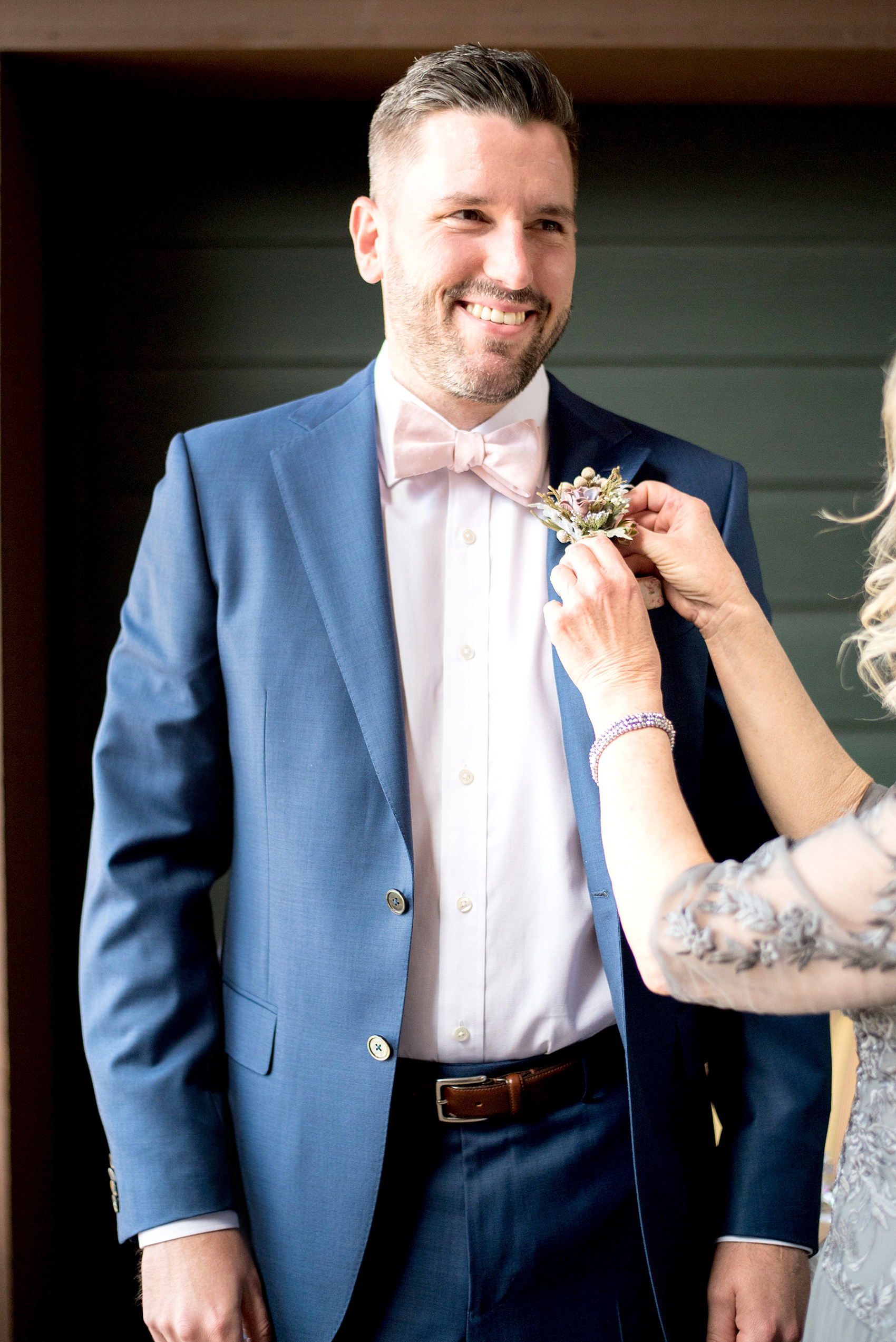 Crystal Springs Resort wedding photos in New Jersey, with photographer Mikkel Paige Photography. The couple’s spring wedding had an outdoor ceremony with photos at this rustic, woodsy venue showing their blue and pink palette decor from getting ready to their reception. This picture shows the groom and his mother pinning on his succulent boutonnieres wrapped with raffia and burlap. Click through to see their complete wedding recap! #NewJerseywedding #MikkelPaige #NJweddingphotographer #NJphotographer #succulents #succulentboutonniere #groomsboutonniere #boutonniere