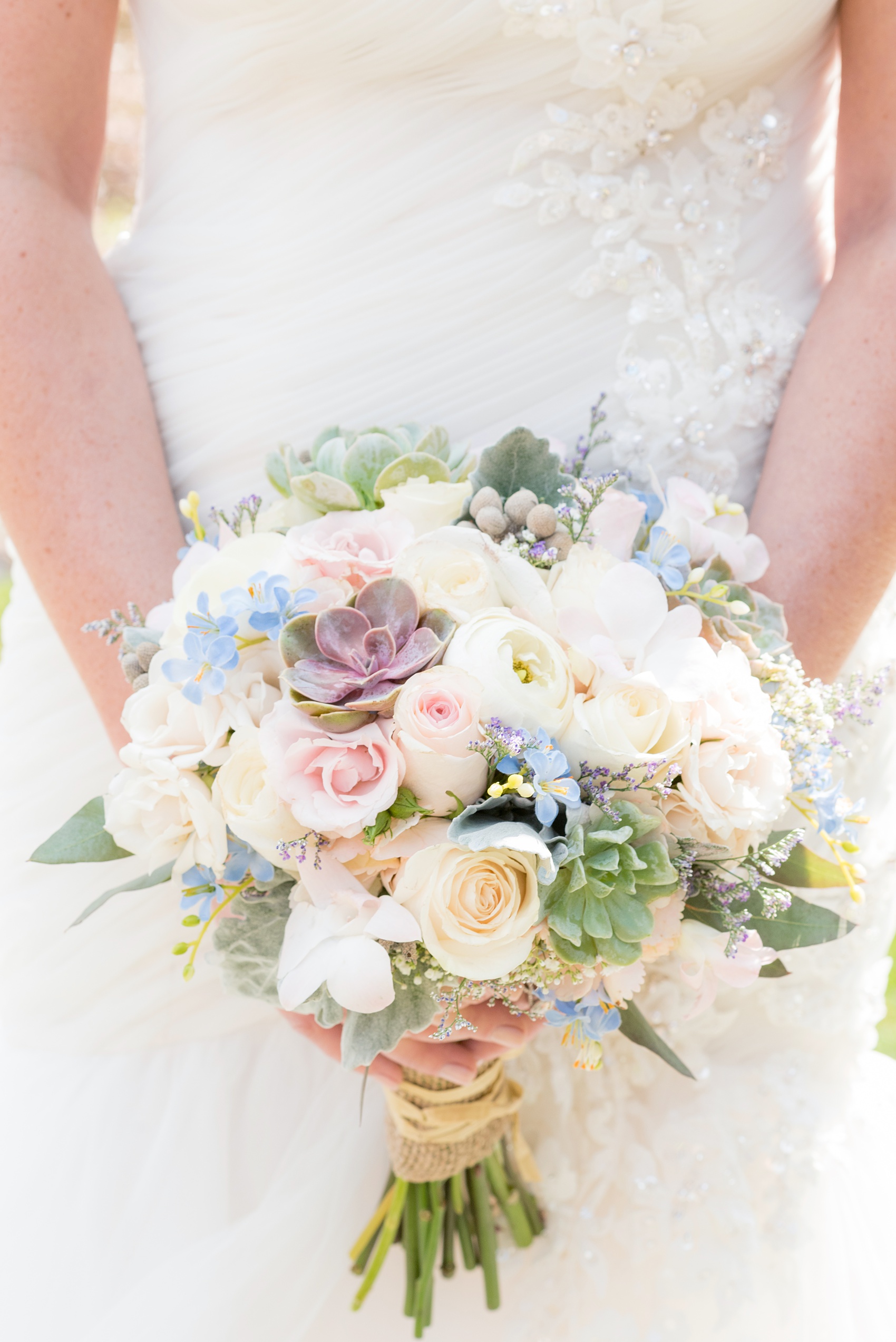 Crystal Springs Resort wedding photos in New Jersey, with photographer Mikkel Paige Photography. The couple’s spring wedding had an outdoor ceremony with photos at this rustic, woodsy venue showing their blue and pink palette decor from getting ready to their reception. This detail picture shows the bride's succulent bouquet, with blue, peach and white flowers and roses, wrapped with raffia and burlap. Click through to see their complete wedding recap! #NewJerseywedding #MikkelPaige #NJweddingphotographer #NJphotographer #succulents #succulentbouquet #weddingflowers #bridalbouquet #springbouquet 