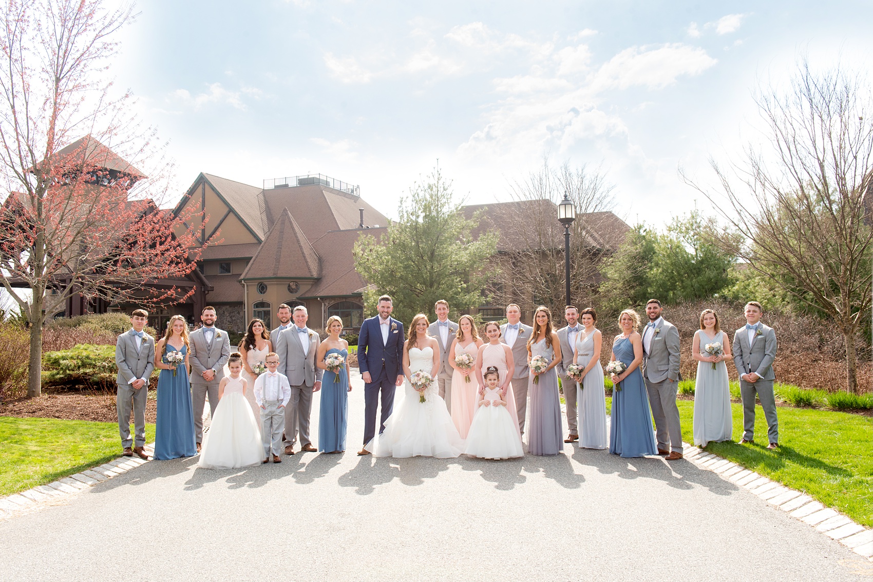 Crystal Springs Resort wedding photos in New Jersey, with photographer Mikkel Paige Photography. The couple’s spring wedding had an outdoor ceremony with photos at this rustic, woodsy venue showing their blue and pink palette decor from getting ready to their reception. This picture shows the complete wedding party: the groomsmen in their grey suits and bridal party (bridesmaids) in their mismatched blue and pink gowns. Click through to see their complete wedding recap! #NewJerseywedding #MikkelPaige #NJweddingphotographer #NJphotographer #brideandgroom #springwedding #mismatchedgowns #pinkandblue #weddingparty #bridalparty