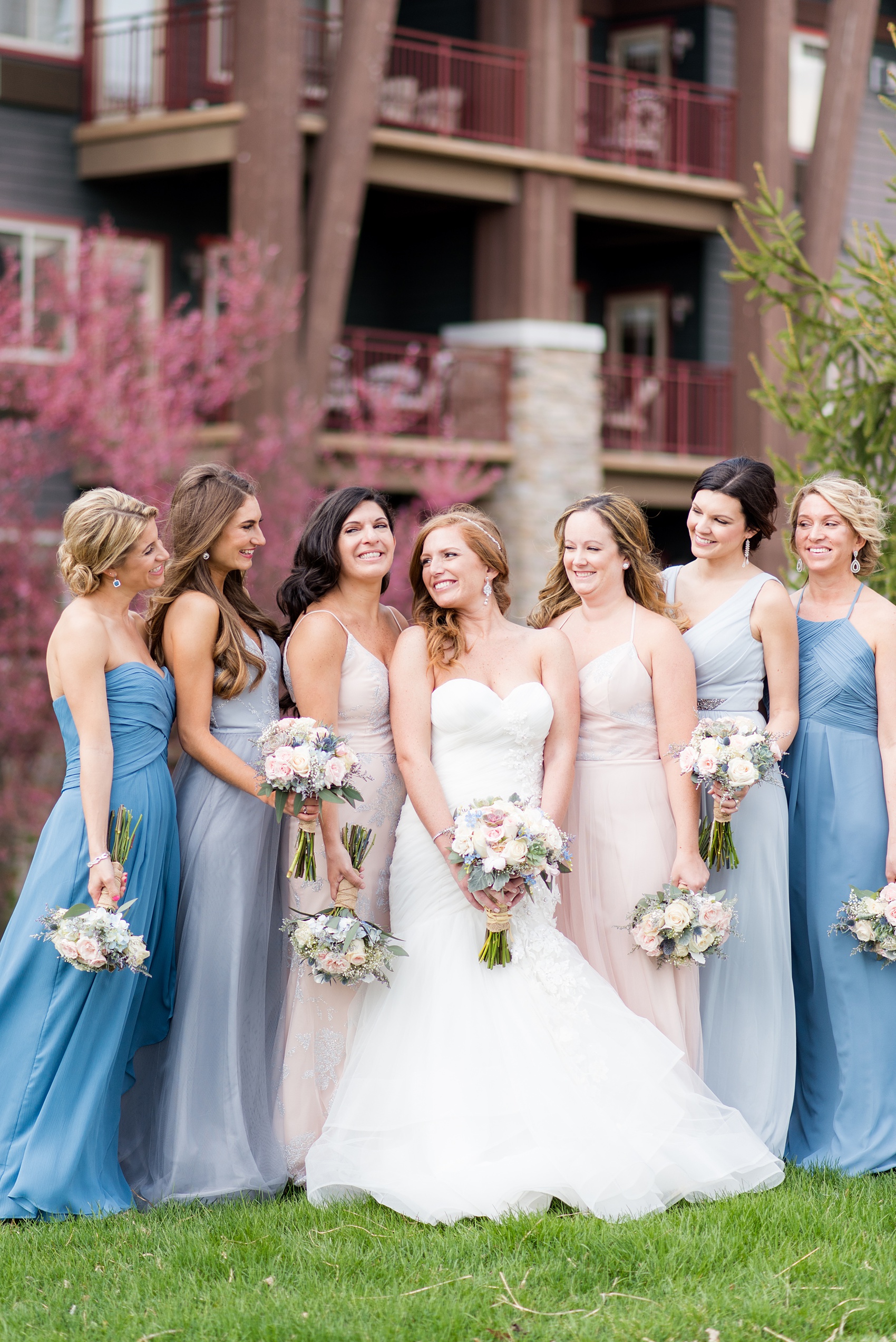 Crystal Springs Resort wedding photos in New Jersey, with photographer Mikkel Paige Photography. The couple’s spring wedding had an outdoor ceremony with photos at this rustic, woodsy venue showing their blue and pink palette decor from getting ready to their reception. This picture shows the bridal party (bridesmaids) in their mismatched blue and pink gowns with cherry blossoms behind them. Click through to see their complete wedding recap! #NewJerseywedding #MikkelPaige #NJweddingphotographer #NJphotographer #brideandgroom #springwedding #mismatchedgowns #pinkandblue #weddingparty #bridalparty