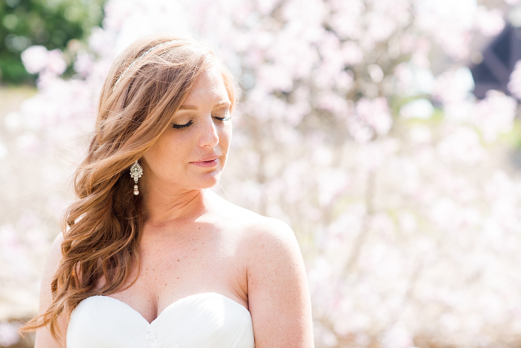 Crystal Springs Resort wedding photos in New Jersey, with photographer Mikkel Paige Photography. The couple’s spring wedding had an outdoor ceremony with photos at this rustic, woodsy venue showing their blue and pink palette decor from getting ready to their reception. This picture shows the bride's side hair do and strapless wedding gown amongst the Cherry Blossoms. Click through to see their complete wedding recap! #NewJerseywedding #MikkelPaige #NJweddingphotographer #NJphotographer #brideandgroom #springwedding #mismatchedgowns #pinkandblue #bridalportrait #bride #CherryBlossoms