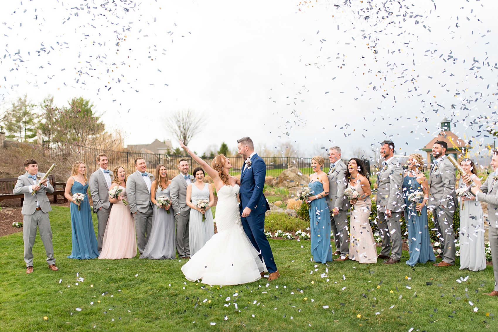 Crystal Springs Resort wedding photos in New Jersey, with photographer Mikkel Paige Photography. The couple’s spring wedding had an outdoor ceremony with photos at this rustic, woodsy venue showing their blue and pink palette decor from getting ready to their reception. This picture shows the complete wedding party: the groomsmen in their grey suits and bridal party (bridesmaids) in their mismatched blue and pink gowns popping confetti to celebrate the day! Click through to see their complete wedding recap! #NewJerseywedding #MikkelPaige #NJweddingphotographer #NJphotographer #brideandgroom #springwedding #mismatchedgowns #pinkandblue #weddingparty #bridalparty