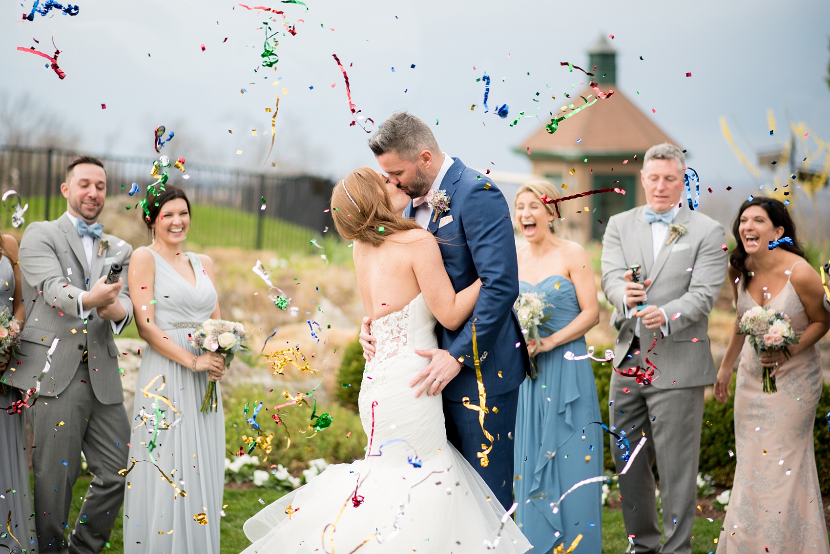 Crystal Springs Resort wedding photos in New Jersey, with photographer Mikkel Paige Photography. The couple’s spring wedding had an outdoor ceremony with photos at this rustic, woodsy venue showing their blue and pink palette decor from getting ready to their reception. This picture shows the complete wedding party: the groomsmen in their grey suits and bridal party (bridesmaids) in their mismatched blue and pink gowns popping confetti to celebrate the day! Click through to see their complete wedding recap! #NewJerseywedding #MikkelPaige #NJweddingphotographer #NJphotographer #brideandgroom #springwedding #mismatchedgowns #pinkandblue #weddingparty #bridalparty