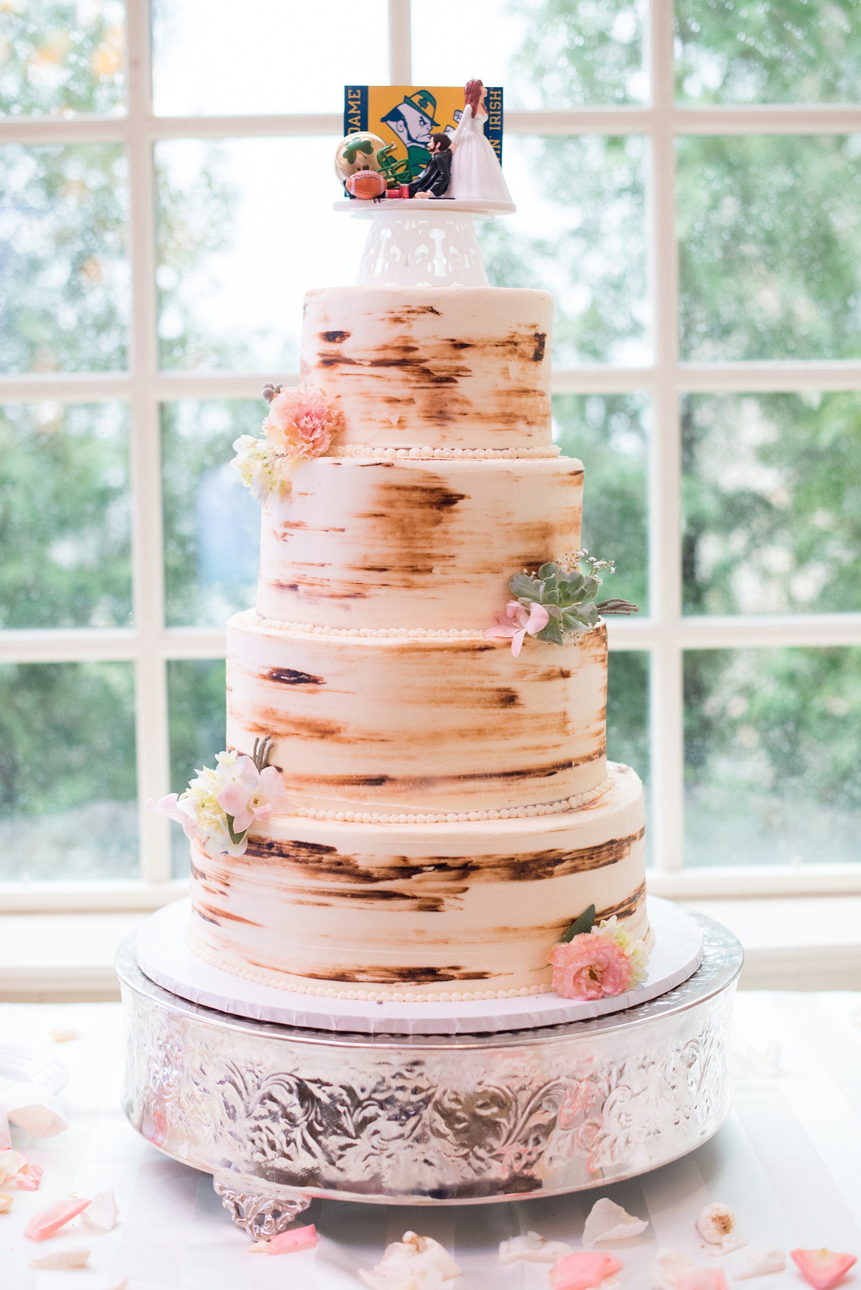 Crystal Springs Resort wedding photos in New Jersey, with photographer Mikkel Paige Photography. The couple’s spring wedding had an outdoor ceremony with photos at this rustic, woodsy venue showing their blue and pink palette decor from getting ready to their reception. This picture shows their tiered "tree" inspiration wedding cake with a Notre Dame football cake topper. Click through to see their complete wedding recap and more inspiration like this! #NewJerseywedding #MikkelPaige #NJweddingphotographer #NJphotographer #springwedding #pinkandblue #treeweddingcake #NotreDameFootball #NotreDame #caketopper