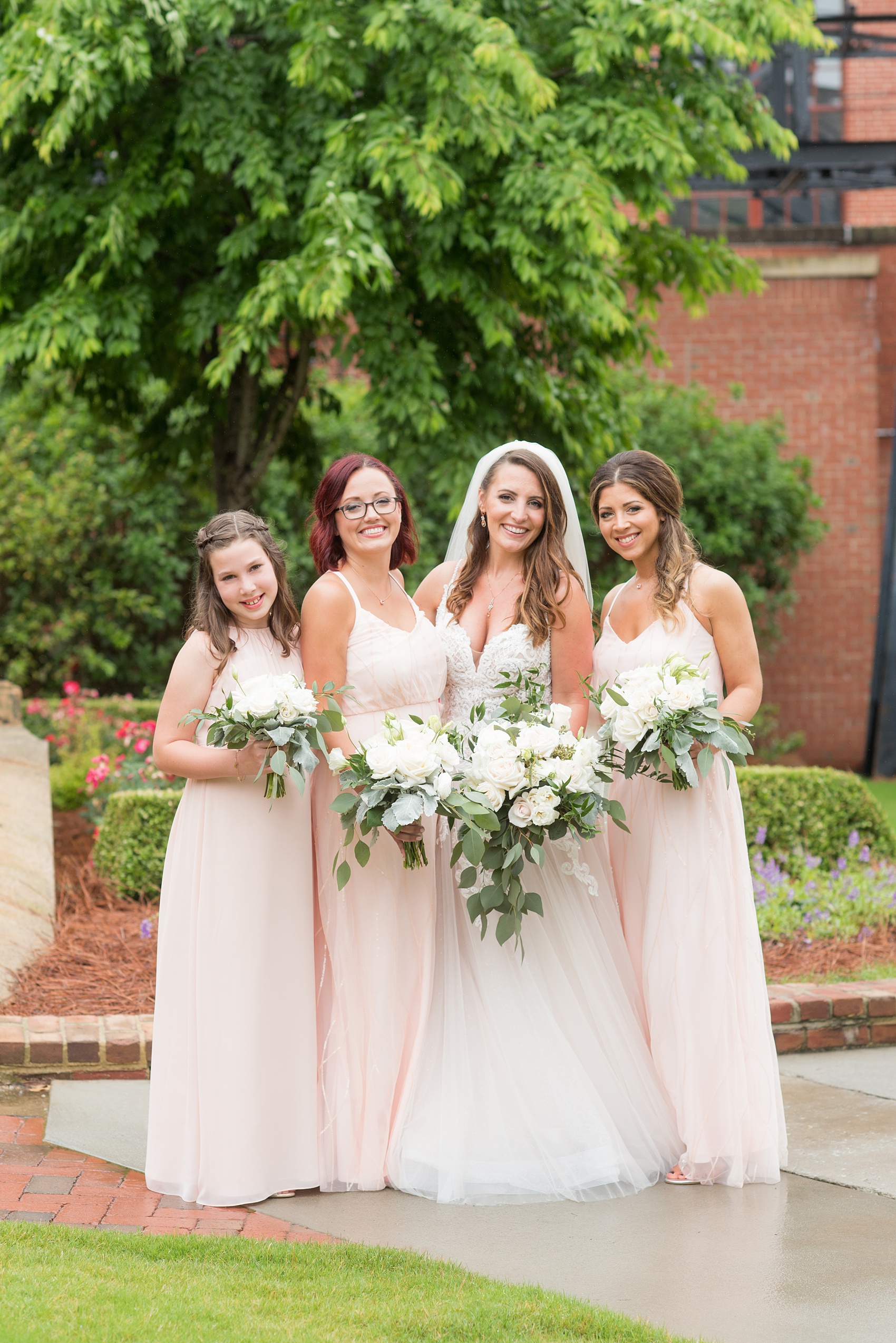 The Rickhouse wedding photos by Mikkel Paige photography in Durham, North Carolina. This urban venue has all the charm of the south for this bride and groom's spring wedding! This picture shows the bridal party posing for a photo with pink gowns and white bouquets at American Tobacco Campus. Click to see more from their day! #mikkelpaige #northcarolina #southernwedding #TheRickhouseDurham #rosegoldandpink #bridalparty #pinkbridesmaids 