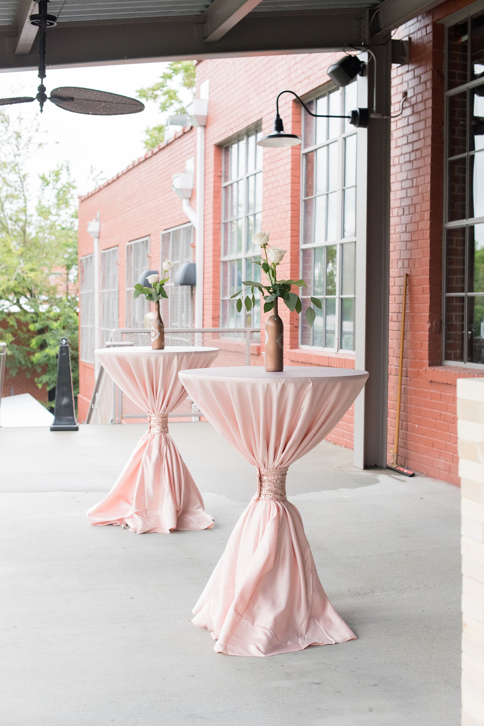 The Rickhouse wedding photos by Mikkel Paige photography in Durham, North Carolina. This urban venue has all the charm of the south for this bride and groom's spring wedding! This picture shows the high tables for cocktail hour dressed in pink linens with bud vases on top. Click to see more from their day! #mikkelpaige #northcarolina #southernwedding #TheRickhouseDurham #rosegoldandpink 