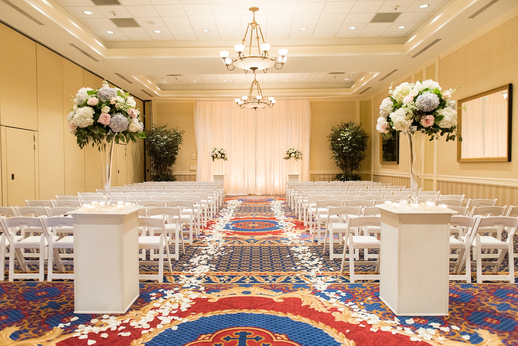 Mikkel Paige Photography pictures of a venue in Durham, North Carolina. The Washington Duke Inn is perfect for a summer wedding! Planning for this beautiful event was by McLean Events. Their ceremony was indoors with white chairs and an aisle lined with white rose petals. Click through for more details about this June wedding with peonies! #MikkelPaige #DurhamWeddings #WashingtonDukeInn #DukeWedding #Duke #McLeanEvents #blueandwhitewedding #indoorceremony #rosepetals