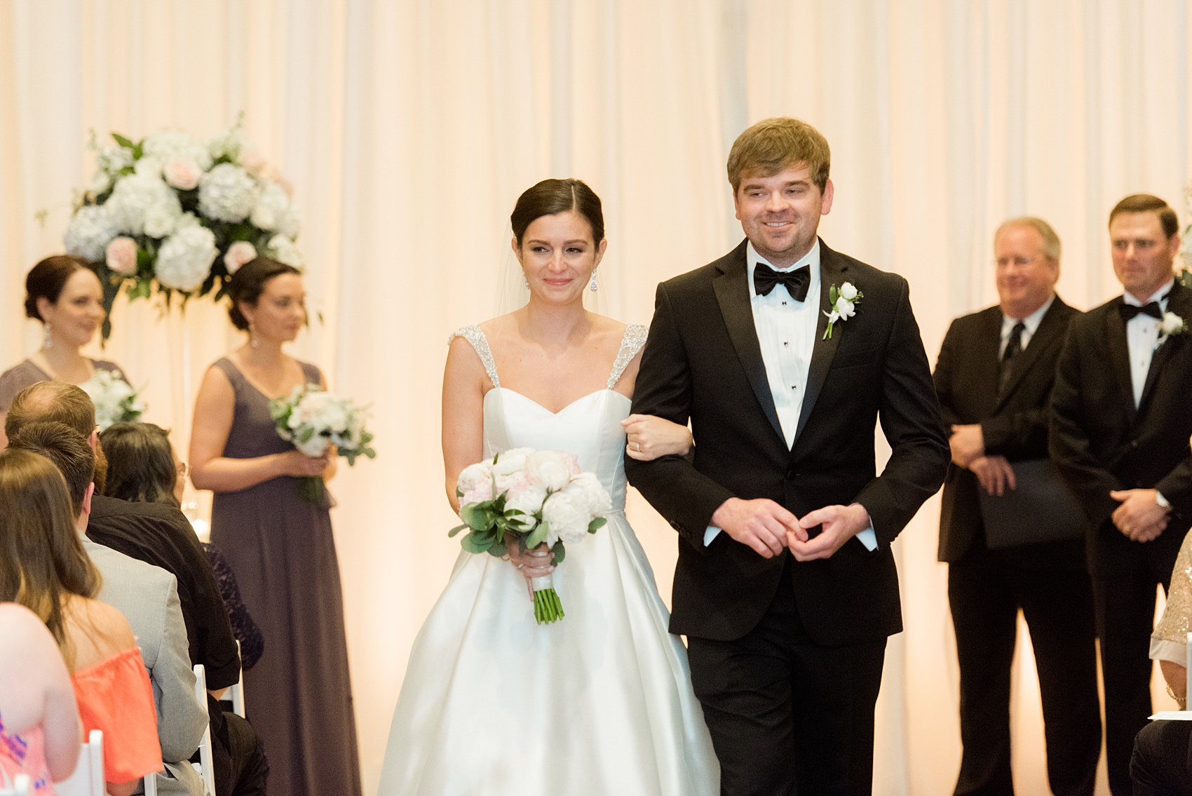 Mikkel Paige Photography pictures of a venue in Durham, North Carolina. The Washington Duke Inn is perfect for a summer wedding! Planning for this beautiful event was by McLean Events. Their ceremony was indoors with white chairs and an aisle lined with white rose petals. Click through for more details about this June wedding with peonies! #MikkelPaige #DurhamWeddings #WashingtonDukeInn #DukeWedding #Duke #McLeanEvents #blueandwhitewedding #indoorceremony #rosepetals