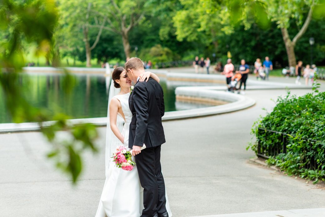 Manhattan Central Park wedding photos by Mikkel Paige Photography at Loeb Boathouse venue. These reception pictures show a timeless couple having fun at their colorful day in this iconic NYC landmark. The bride held a pink peony bouquet for their June celebration and wore a boat-neck gown with buttons down the back and the groom a black suit. Click through for the complete post! #CentralParkWeddingVenues #NYCweddingphotographer #NYCwedding #SummerWedding #CentralParkPhotos #NYbrideandgroom