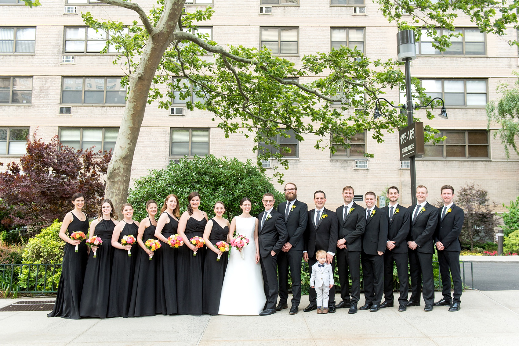 Manhattan Central Park wedding photos by Mikkel Paige Photography at Loeb Boathouse venue. These ceremony and reception pictures show a timeless couple having fun at their colorful day with guests who traveled in from abroad. The bride and groom took their pictures on the Upper West Side with the bridal party. The bridesmaids wore mismatched long black chiffon dresses and groomsmen wore black suits and dark Penguin ties for their June celebration. Colorful flowers and a peony bouquet brightened the scene with a pop of color. Click through for the complete post! #CentralParkWeddingVenues #NYCweddingphotographer #NYCwedding #SummerWedding #ClassicGroomsmen #BlackBridesmaidsGowns #ColorfulBouquets #PeoniesBouquet