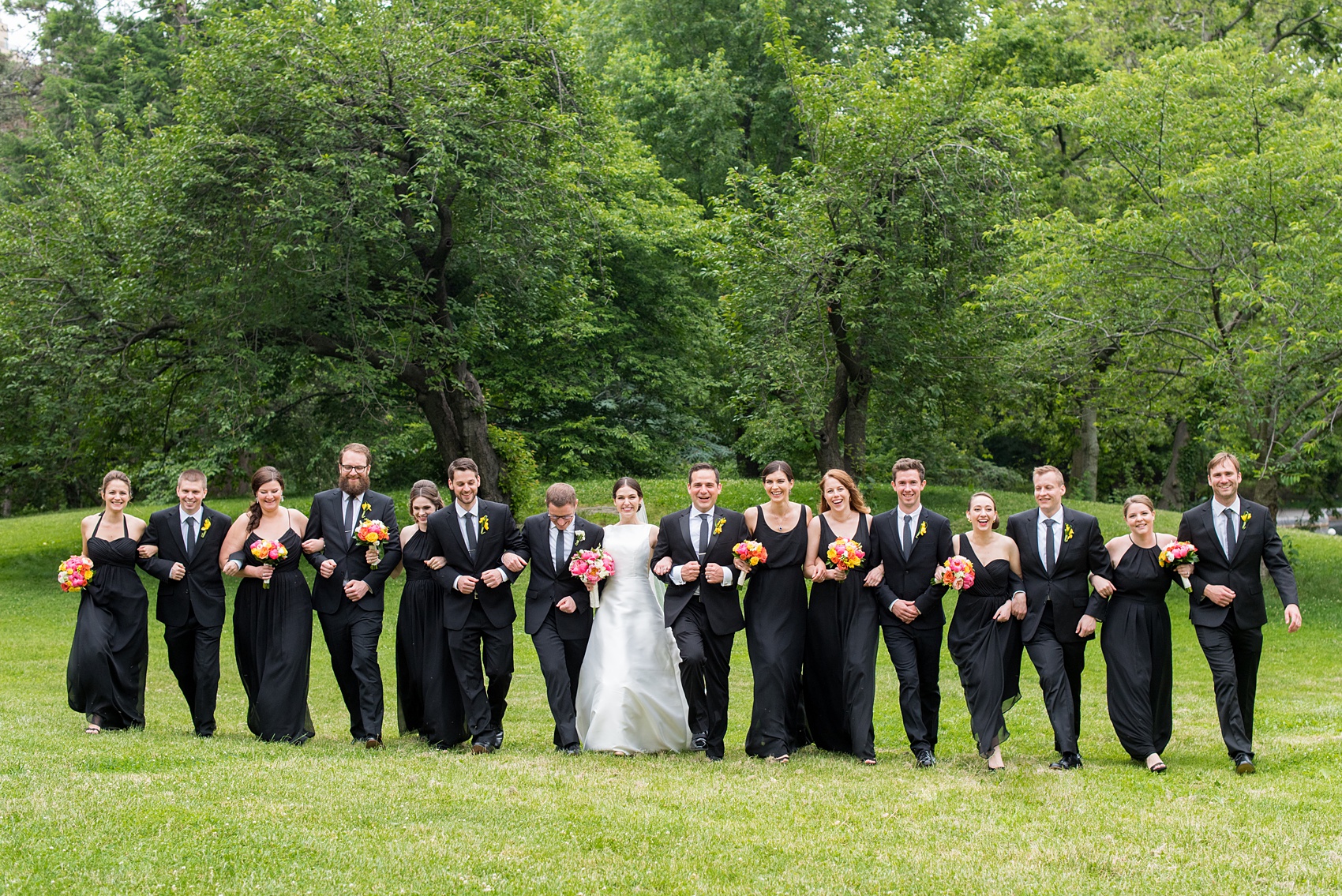 Manhattan Central Park wedding photos by Mikkel Paige Photography at Loeb Boathouse venue. The bride and groom took their pictures on the lawn with the bridal party. The bridesmaids wore mismatched long black chiffon dresses and groomsmen black suits with dark ties. Colorful flowers and a peony bouquet brightened the scene with pops of color. Click through for the complete post! #CentralParkWeddingVenues #NYCweddingphotographer #NYCwedding #BlackBridesmaidsGowns #ColorfulBouquets #PeoniesBouquet