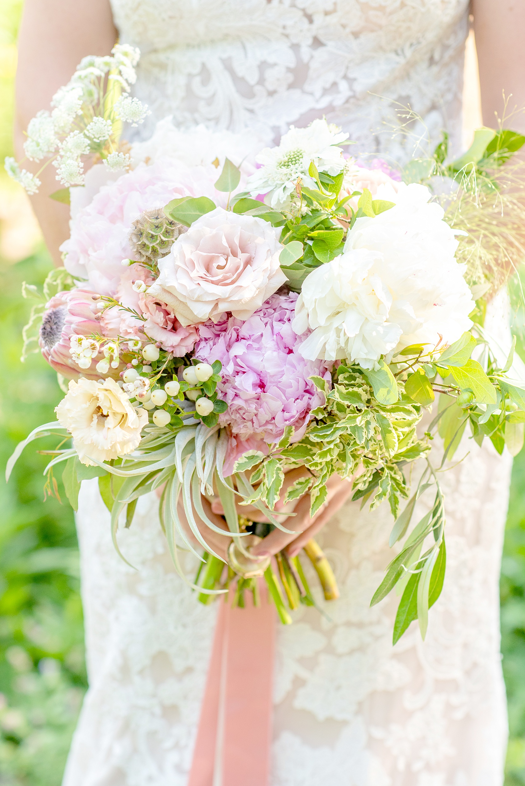 A summer wedding at Olde Mill Inn, NJ. Photos by Mikkel Paige Photography for an event with light pink and blue details. This New Jersey venue is a great option for something not too far from NYC. The bride carried a bouquet of King Protea, peonies, scabiosa pods and assorted garden flowers. The stems were wrapped with colorful ribbon and had a special locket charm on it with photos of family members who had passed away. Click through for their complete wedding recap! #OldeMillInn #NJwedding #NJweddingphotographer #mikkelpaige #NewJerseyWeddingVenue #NewJerseyWedding #CrossEstateGardens #weddingdetails #weddingbouquet #bouquetcharm #peonies #protea